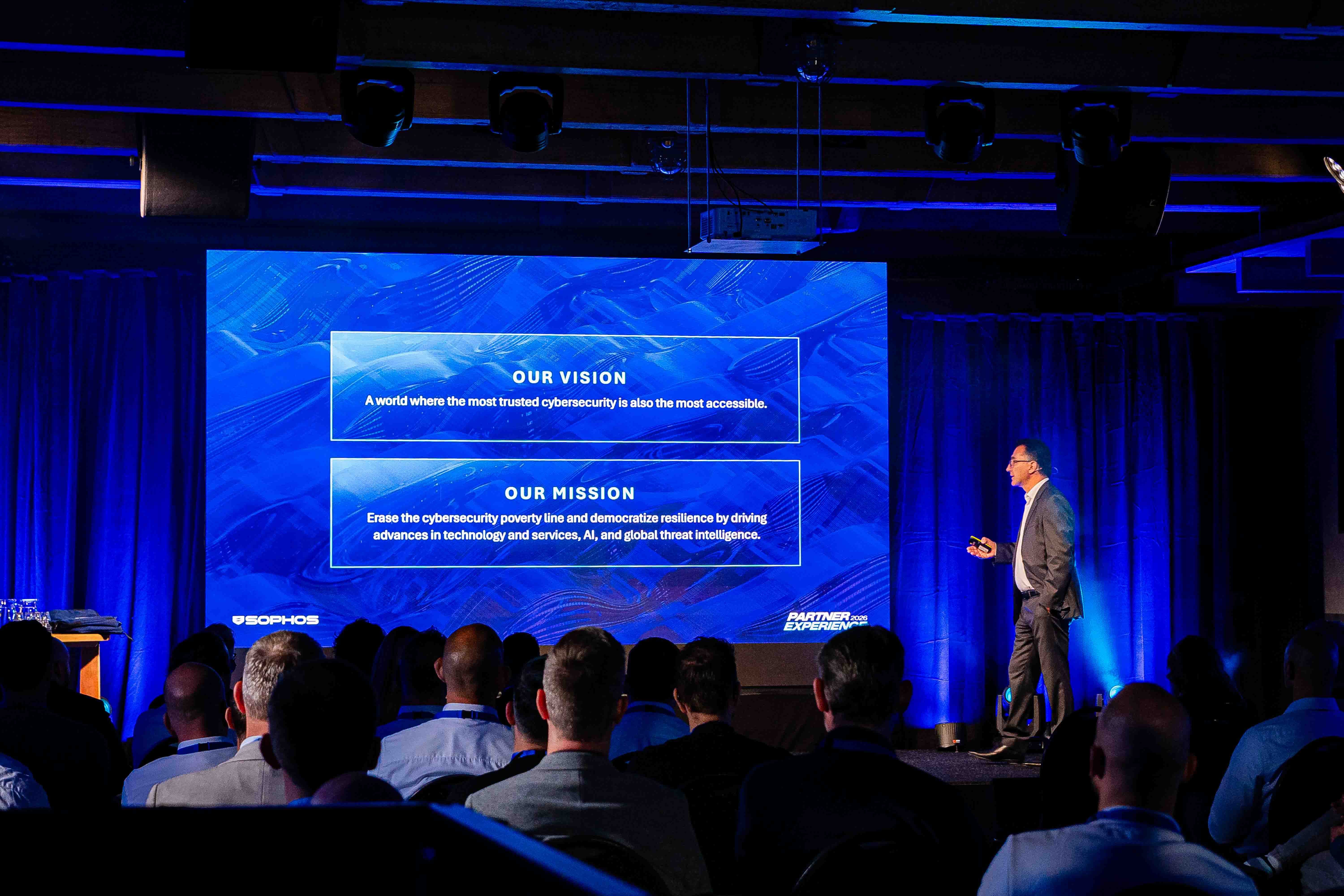 Spreker op het podium met ledwall op de achtergrond tijdens de Sophos Partner Experience