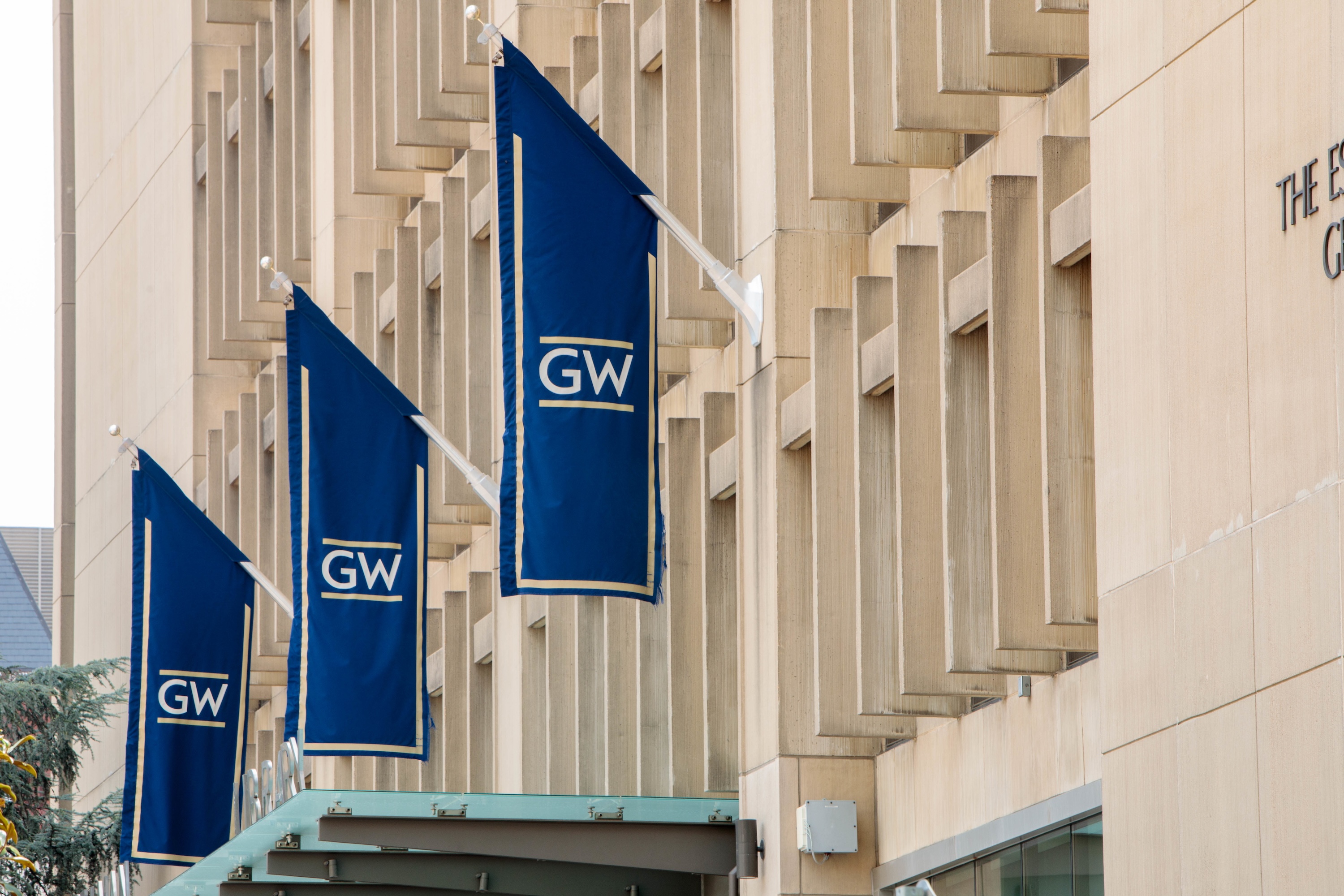 Three blue GW banners hanging on the exterior of a campus building.