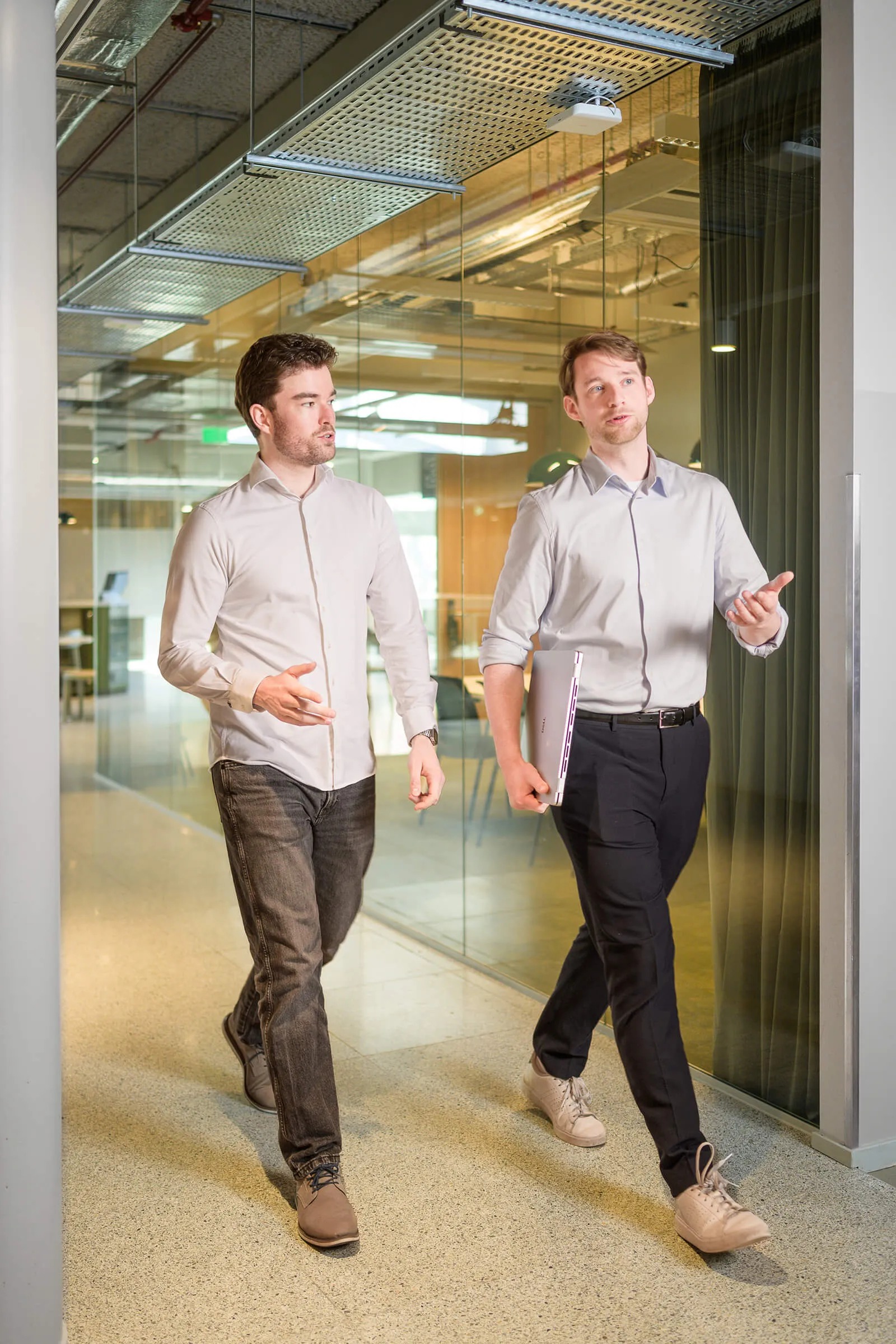 Twee Arxion-consultants lopen pratend door de kantoorgang, één met een laptop onder de arm