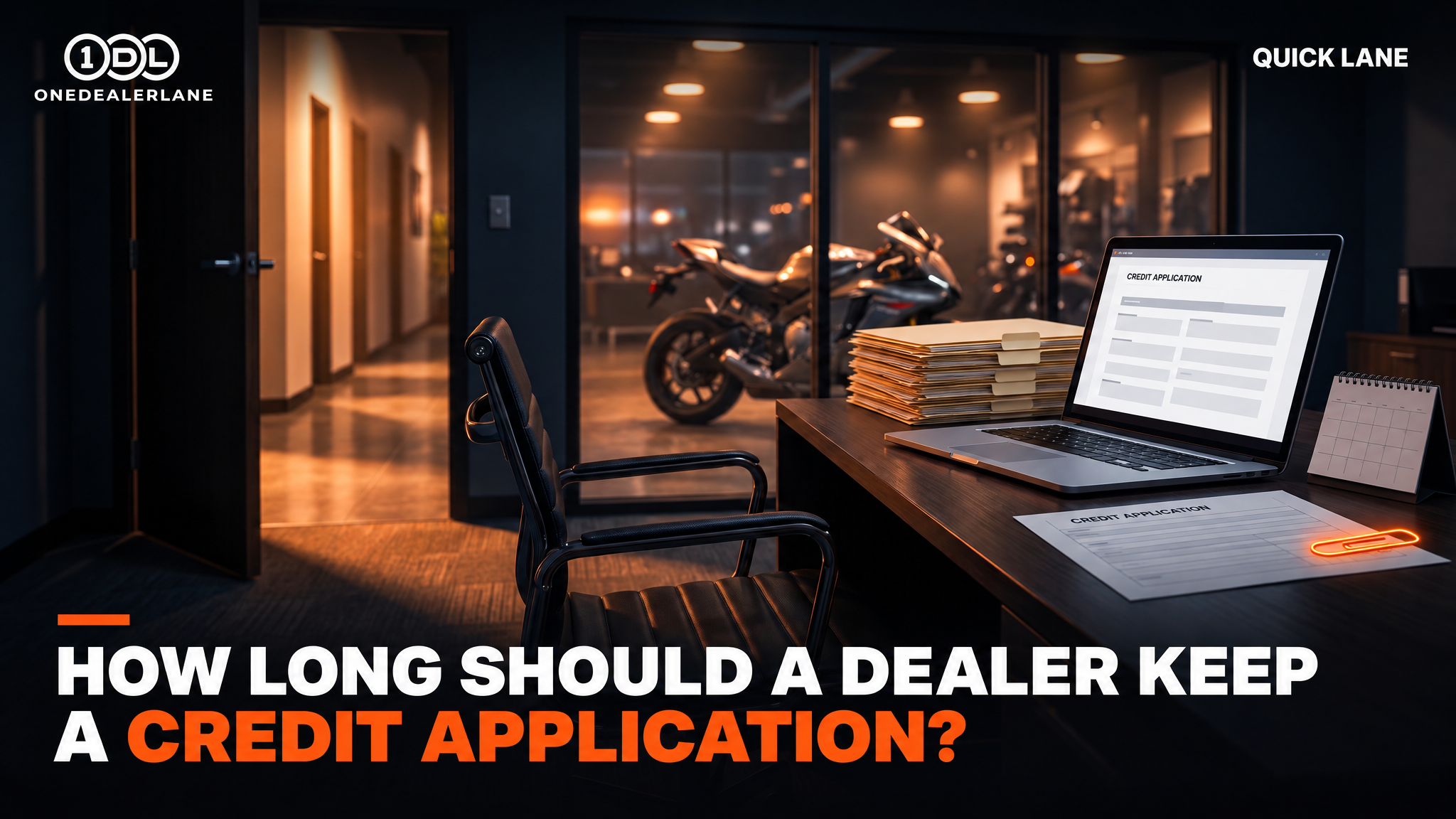 Dealership F&I desk at night with a credit application on a laptop, stacked file folders and a motorcycle in the showroom behind.