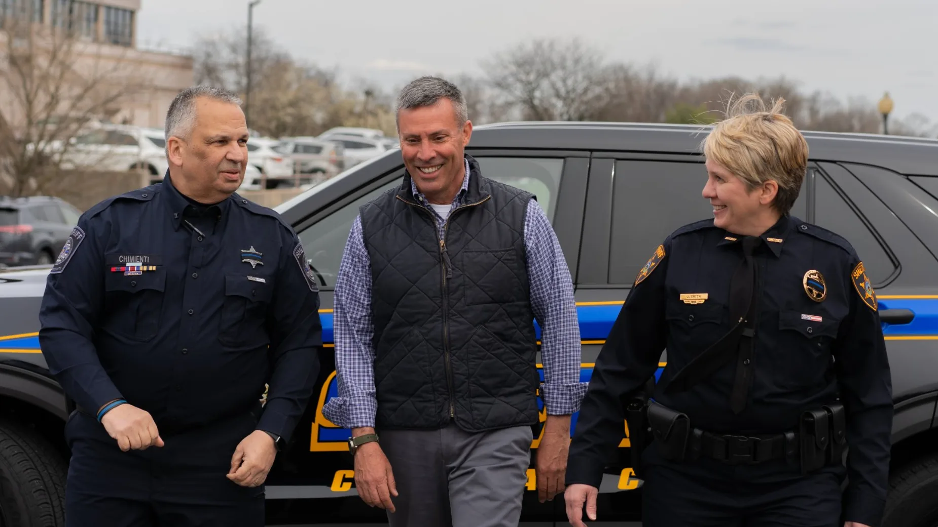 Greg Rothman walking with Dauphin County Sheriff Nicholas Chimienti and former Cumberland County Sheriff Jody Smith beside a sheriff's patrol vehicle.