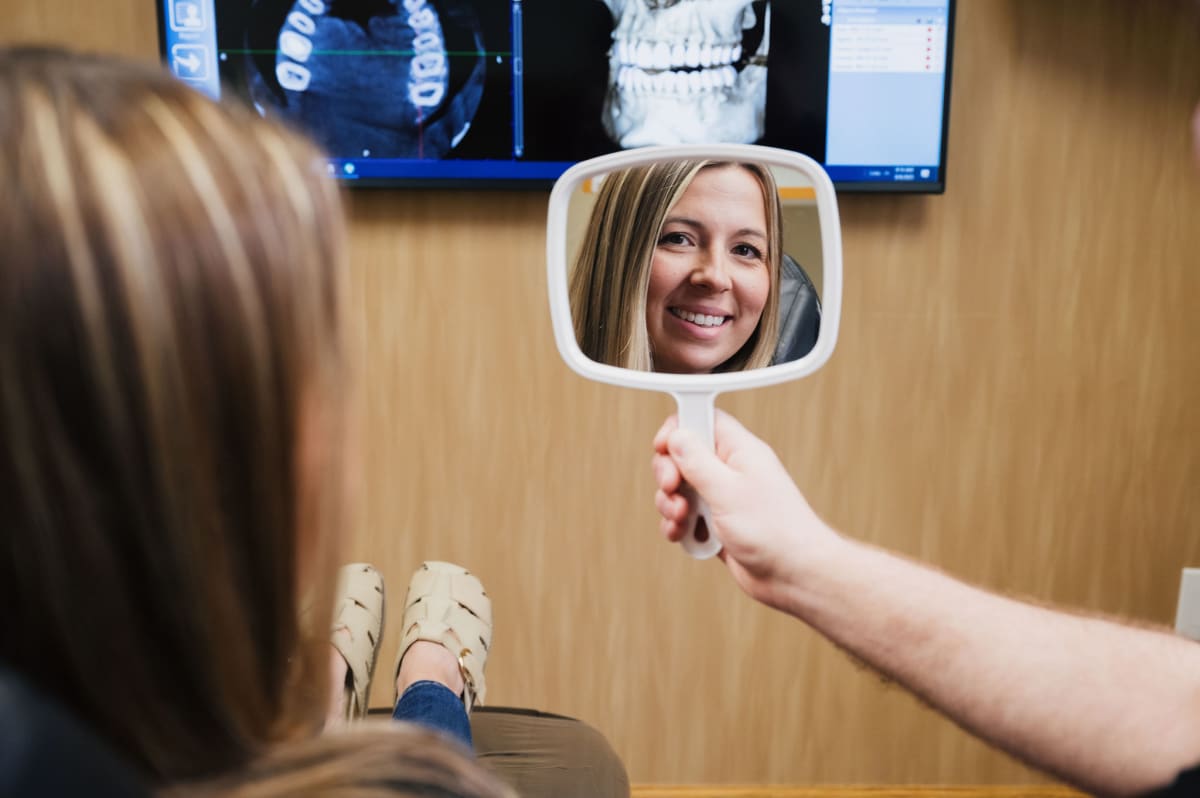 Woman holding handheld mirror to admire her smile in a dental office setting.