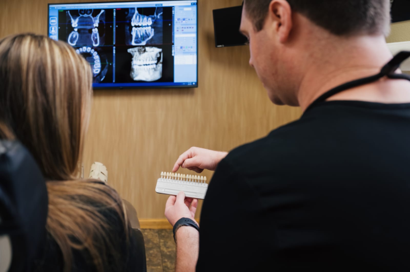 Dentist explaining treatment to patient while pointing at dental x-ray display