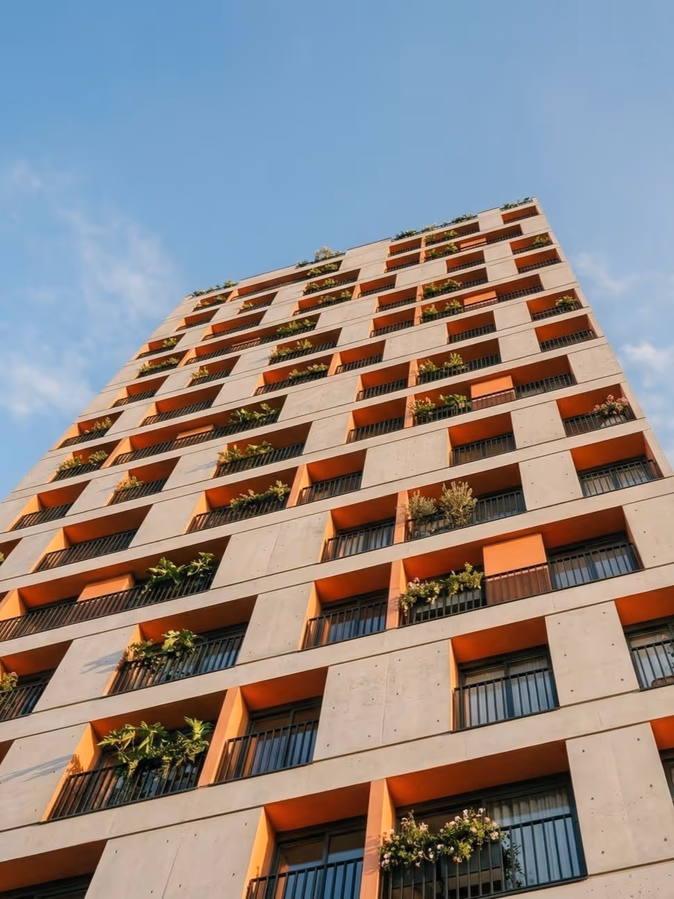 Fachada do Parkside Rio Branco vista de baixo, com varandas em concreto, detalhes em laranja e plantas nas sacadas