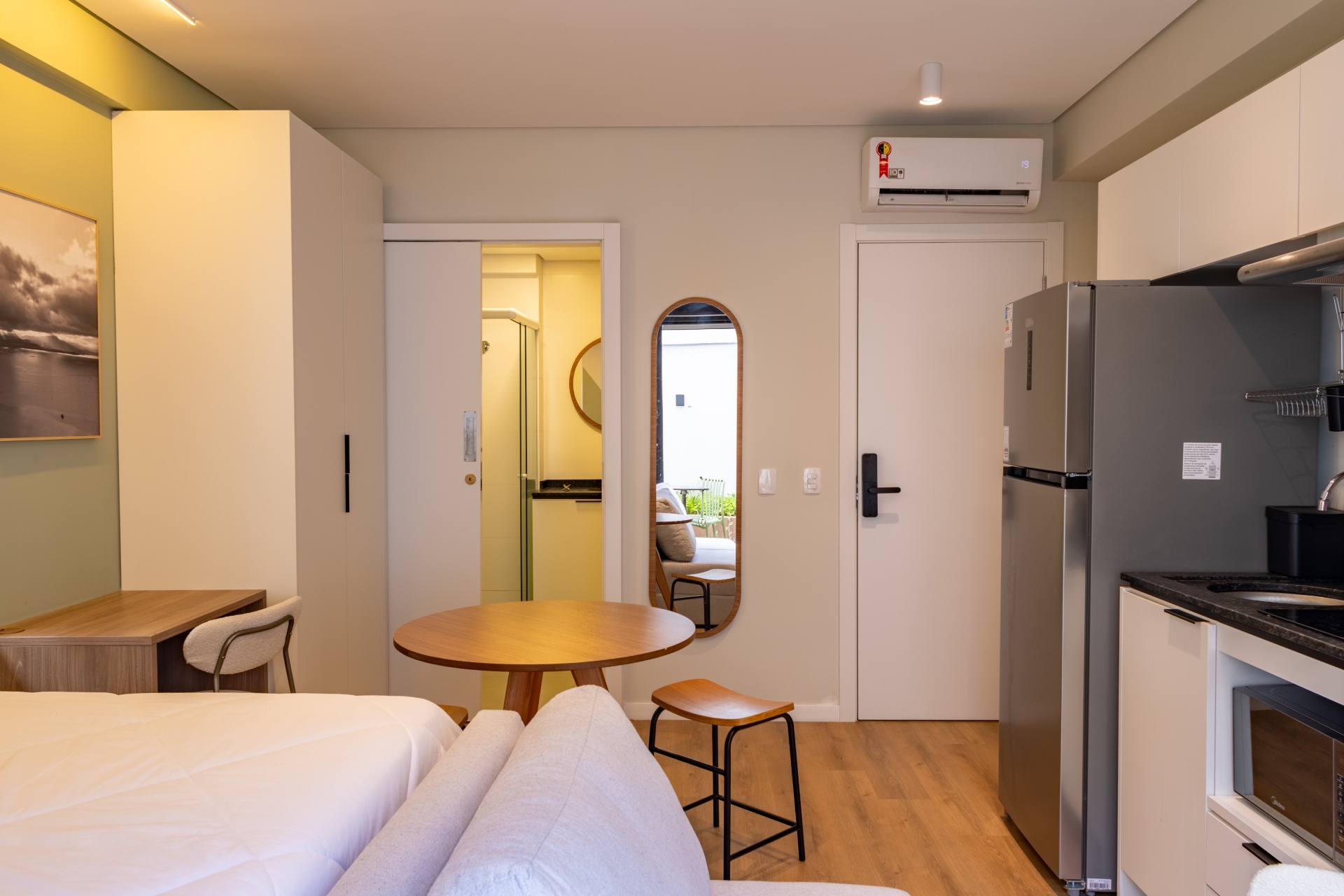 Apartamento mobiliado no Parkside Downtown, localizado no centro de Florianópolis, com ar-condicionado, geladeira, espelho, banheiro, geladeira, armários, bancos e mesa de madeira, pia na cozinha, cama, sofá e outros itens essenciais.