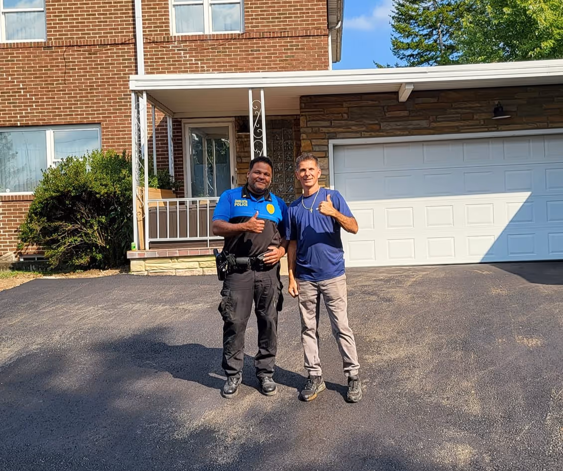 Two men standing in front of a house with a newly paved driveway.