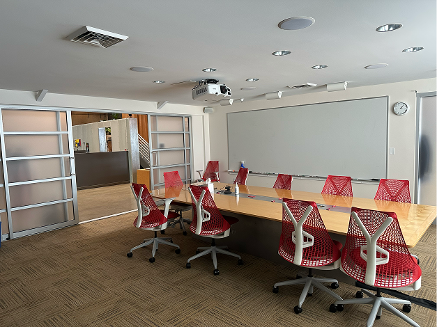 A conference room with a projector screen and red chairs.