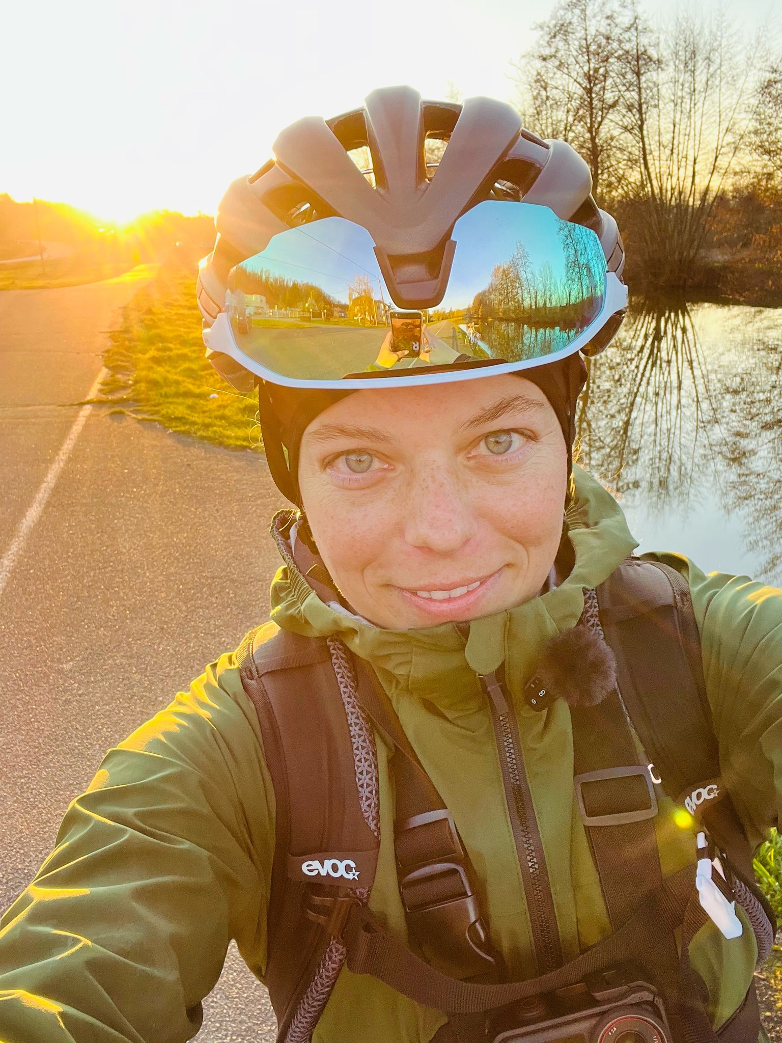 Marie mit einem Helm, eine Radbrille auf dem Helm, bei Sonnenuntergang mit einem Rucksack von vorne.