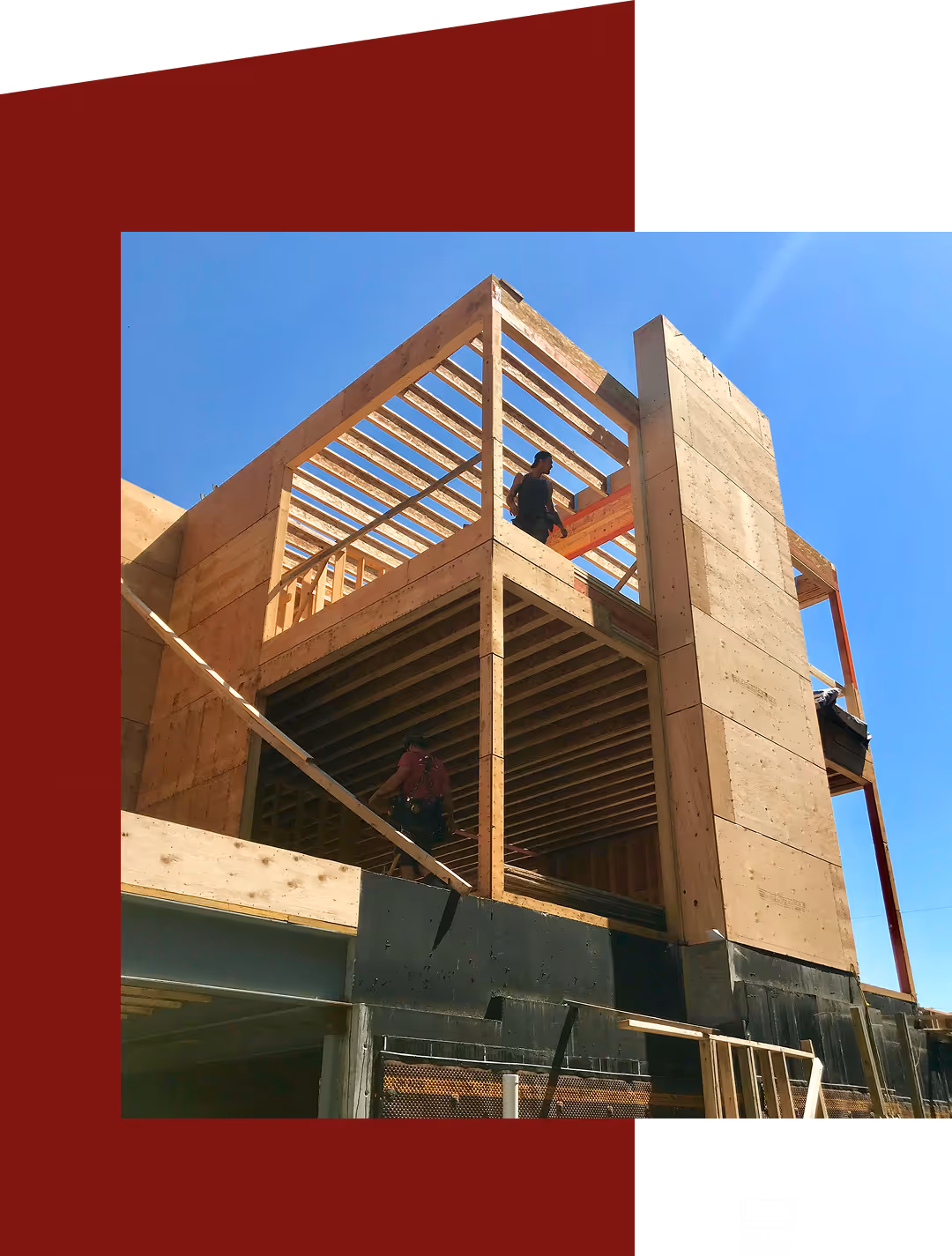 Two workers constructing a multi-story wooden frame building under a clear blue sky.