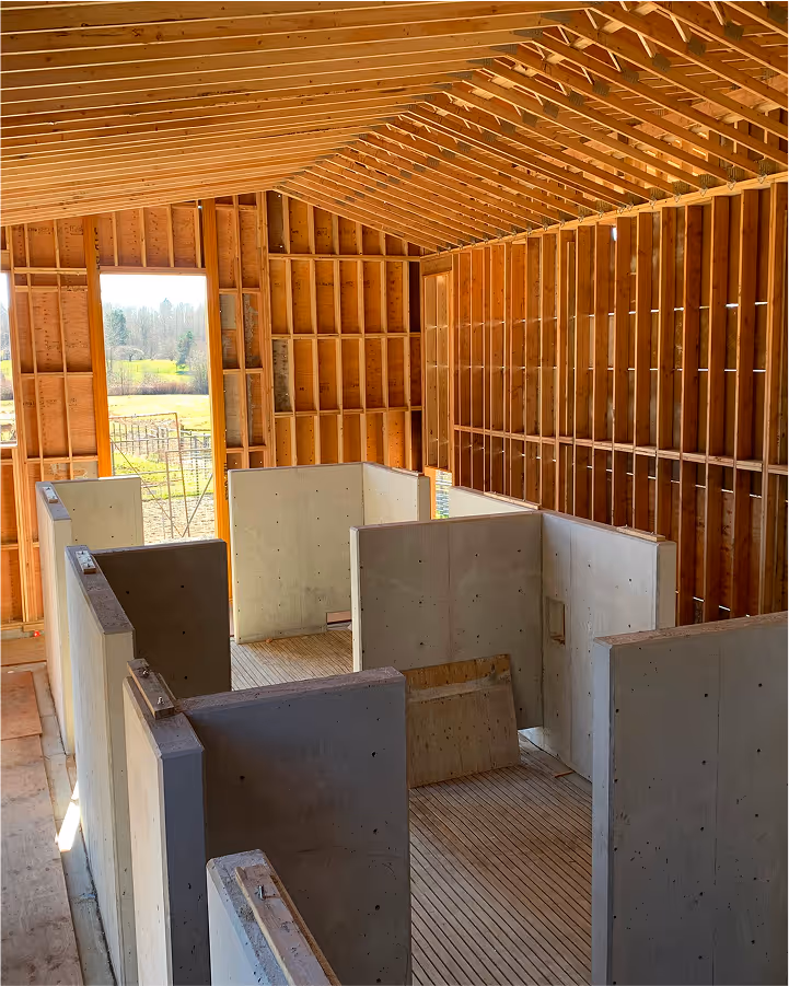 Interior of a wooden framed structure under construction with multiple concrete stall walls inside.