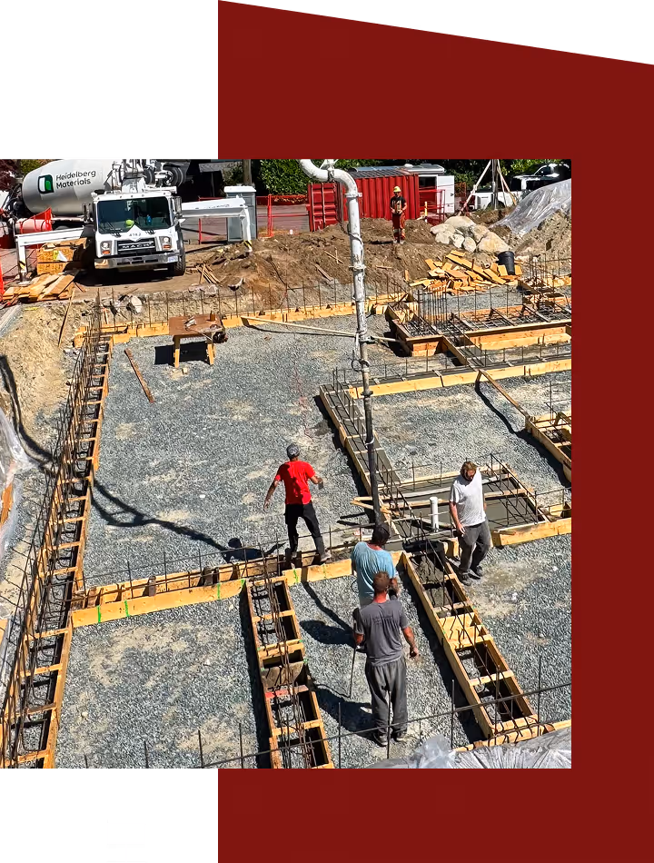 Construction site with four workers preparing foundation framework surrounded by wooden boards and rebar, with a concrete mixer truck in the background.