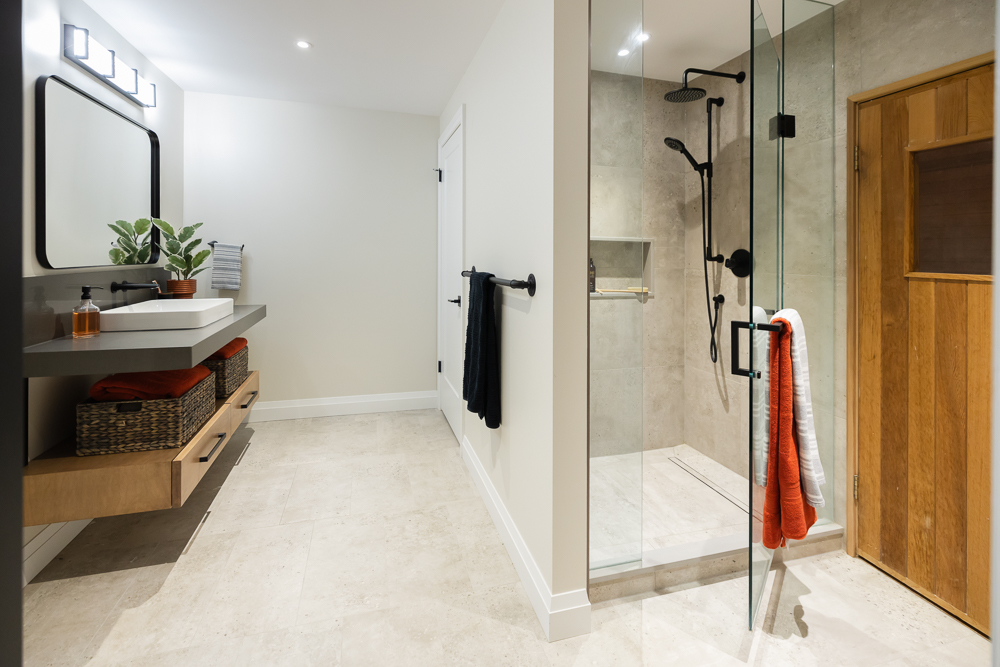 A gorgeous tile floor with the appearance of exposed aggregate concrete and a bespoke floating vanity with both open space for towels or baskets and drawer storage for personal items. Black hardware & accents finish off the industrial theme of this at-home