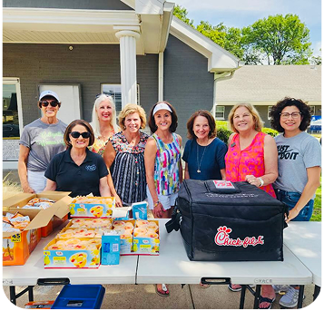 Volunteer group smiling in front of Feed Our Kids lunch line 