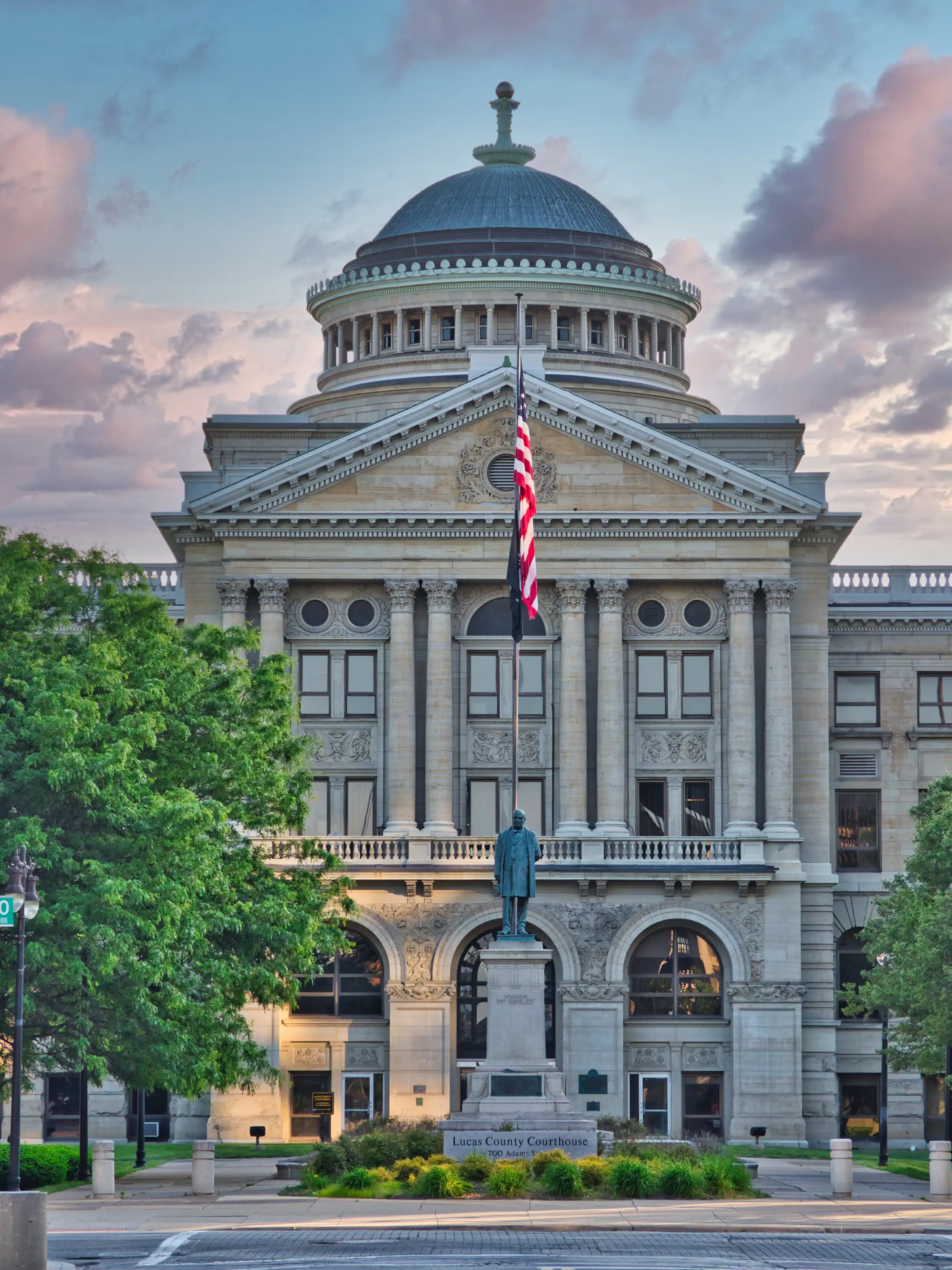 Lucas County Courthouse in Toledo, Ohio, featuring a domed roof, classical stone architecture, and an American flag flying above the entrance.