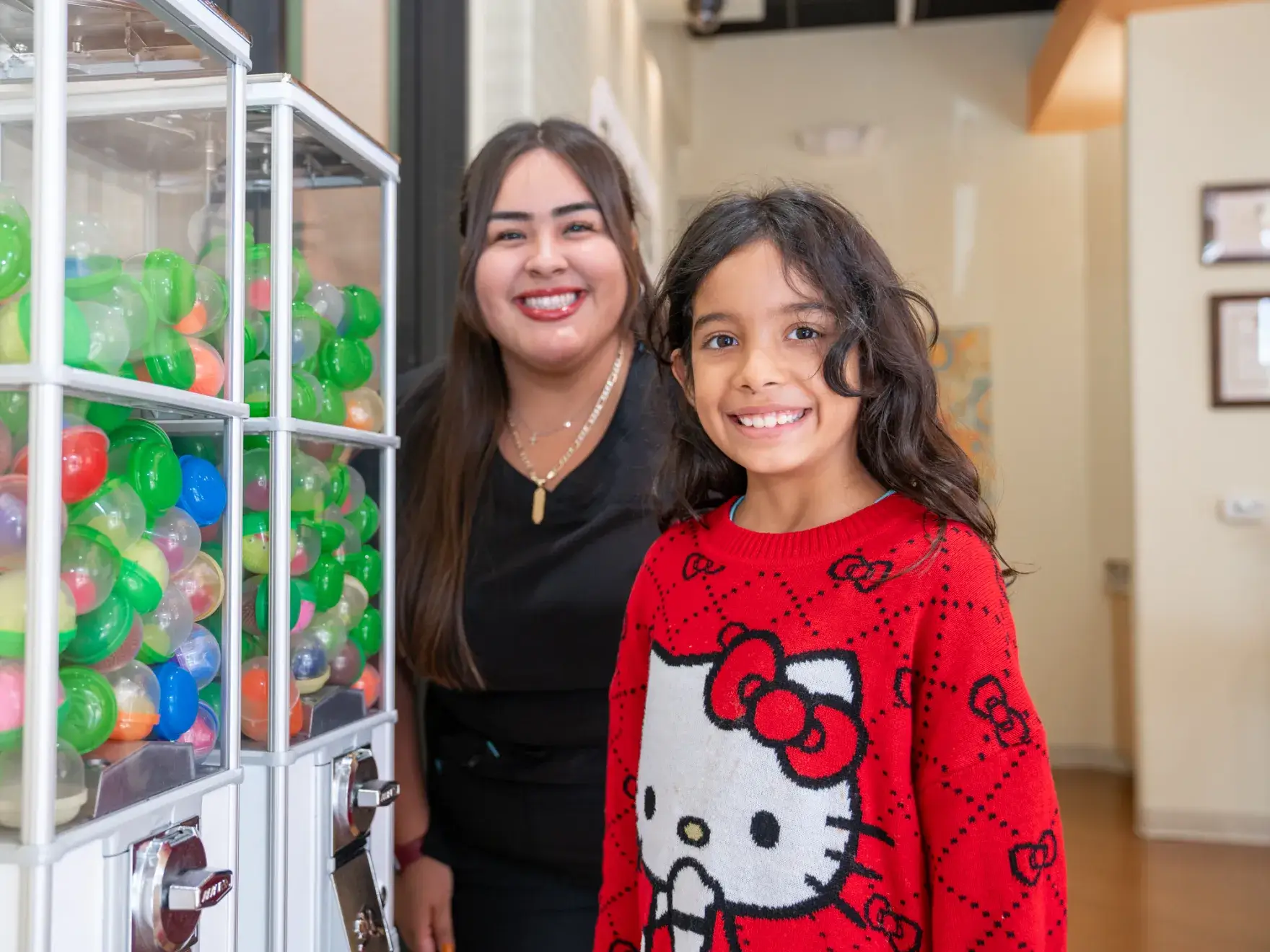 a woman standing next to a little girl in front of a vending machine