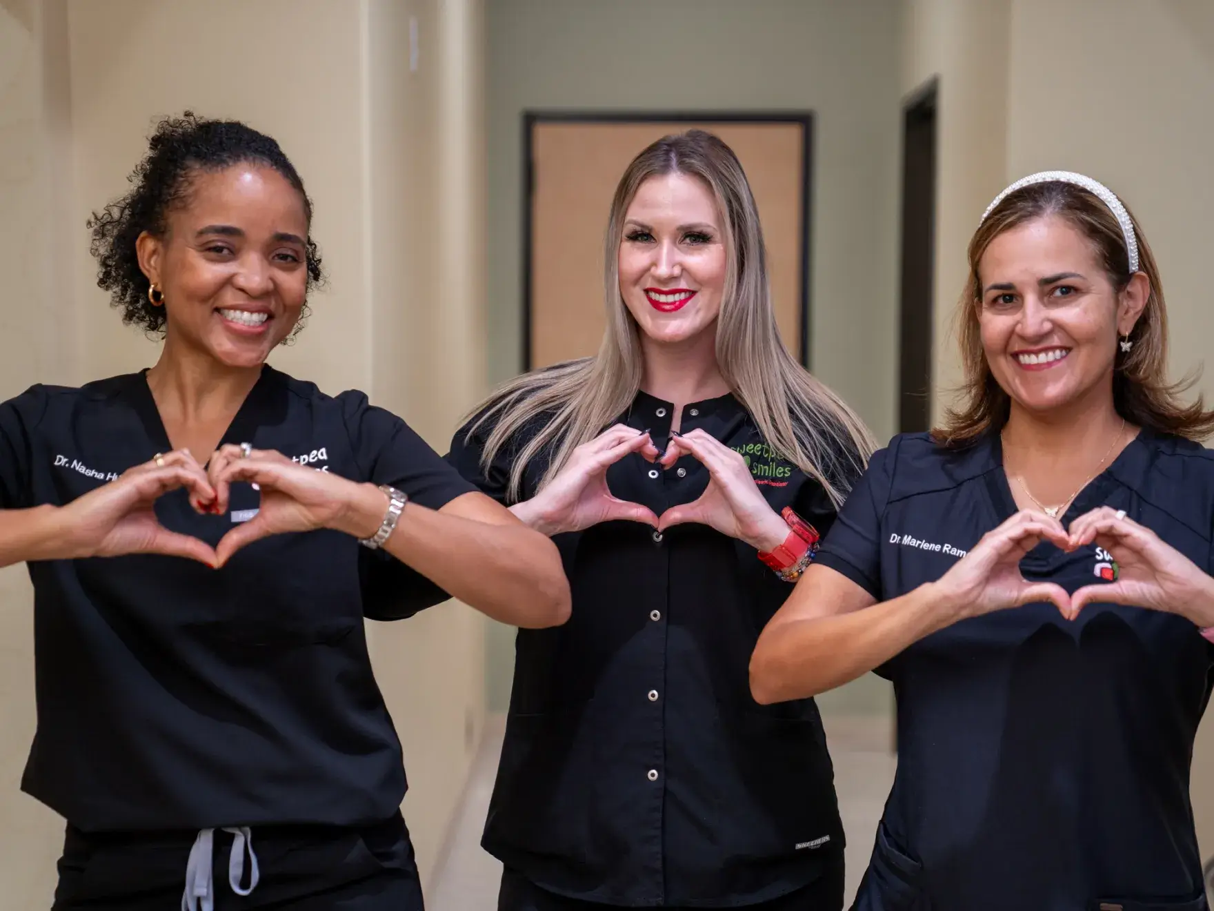 three women in scrubs hold their hands in the shape of a heart