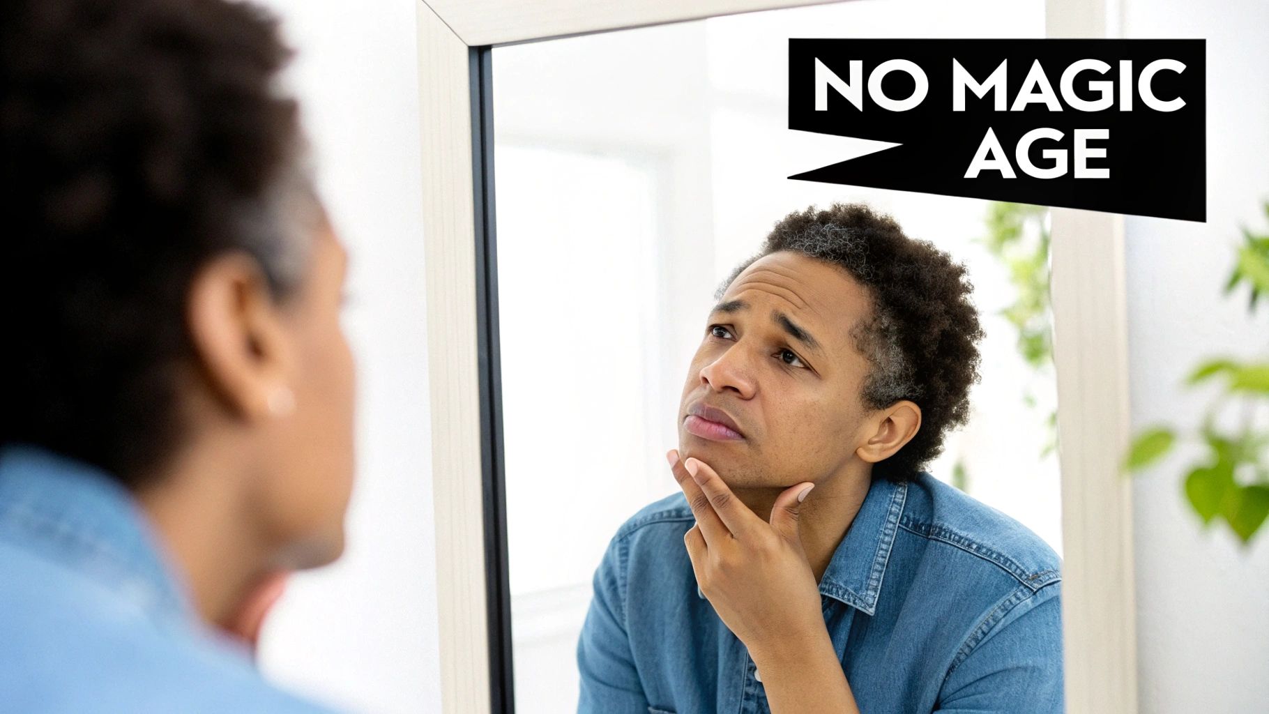 A person with grey hair looks closely at their reflection in a mirror, touching their chin.