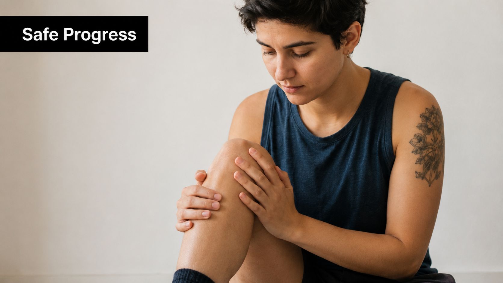 A person with a short haircut gently touching and examining their knee while sitting down.