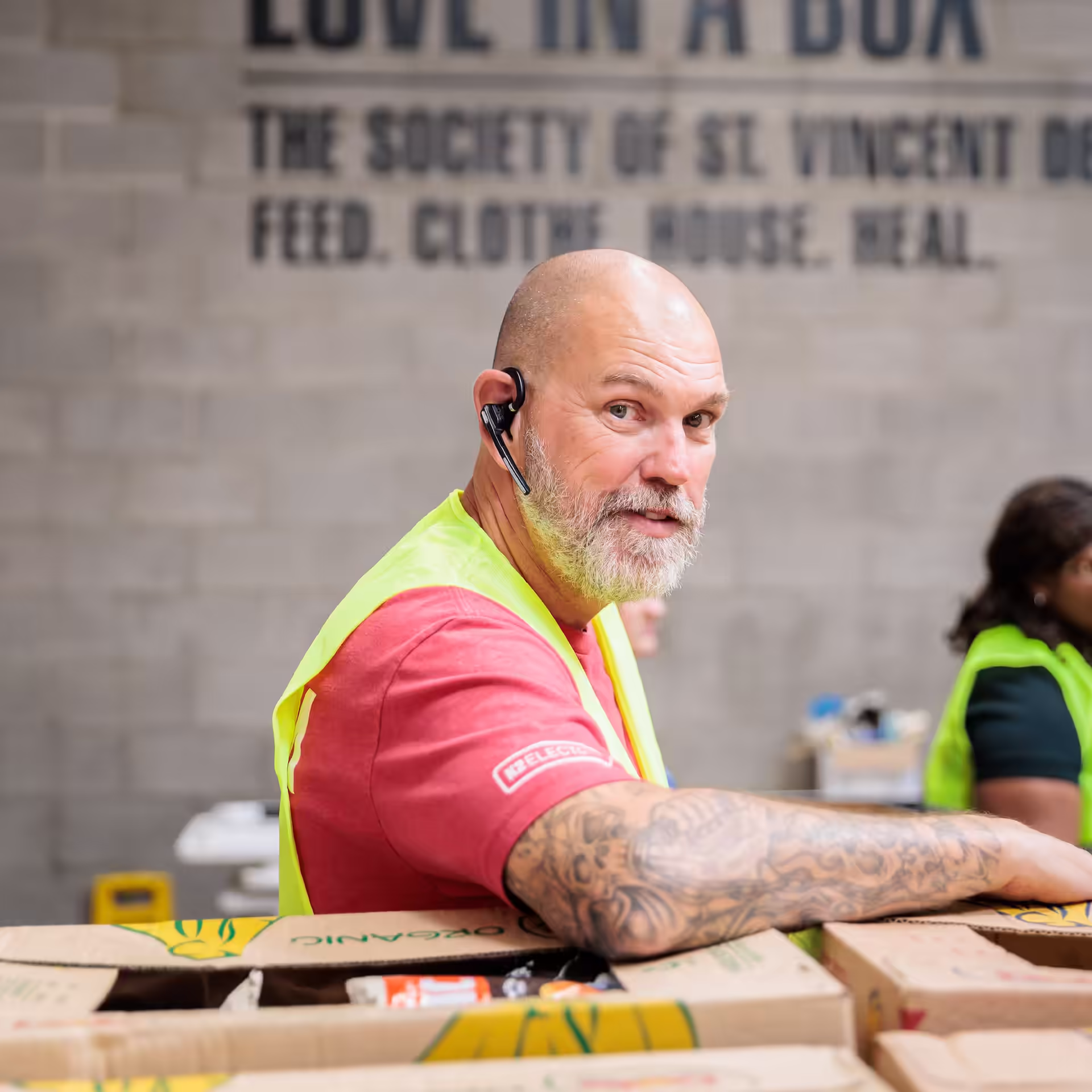 An experienced electrician with the IEC Foundation poses with boxes of food at an IEC-F community service event.