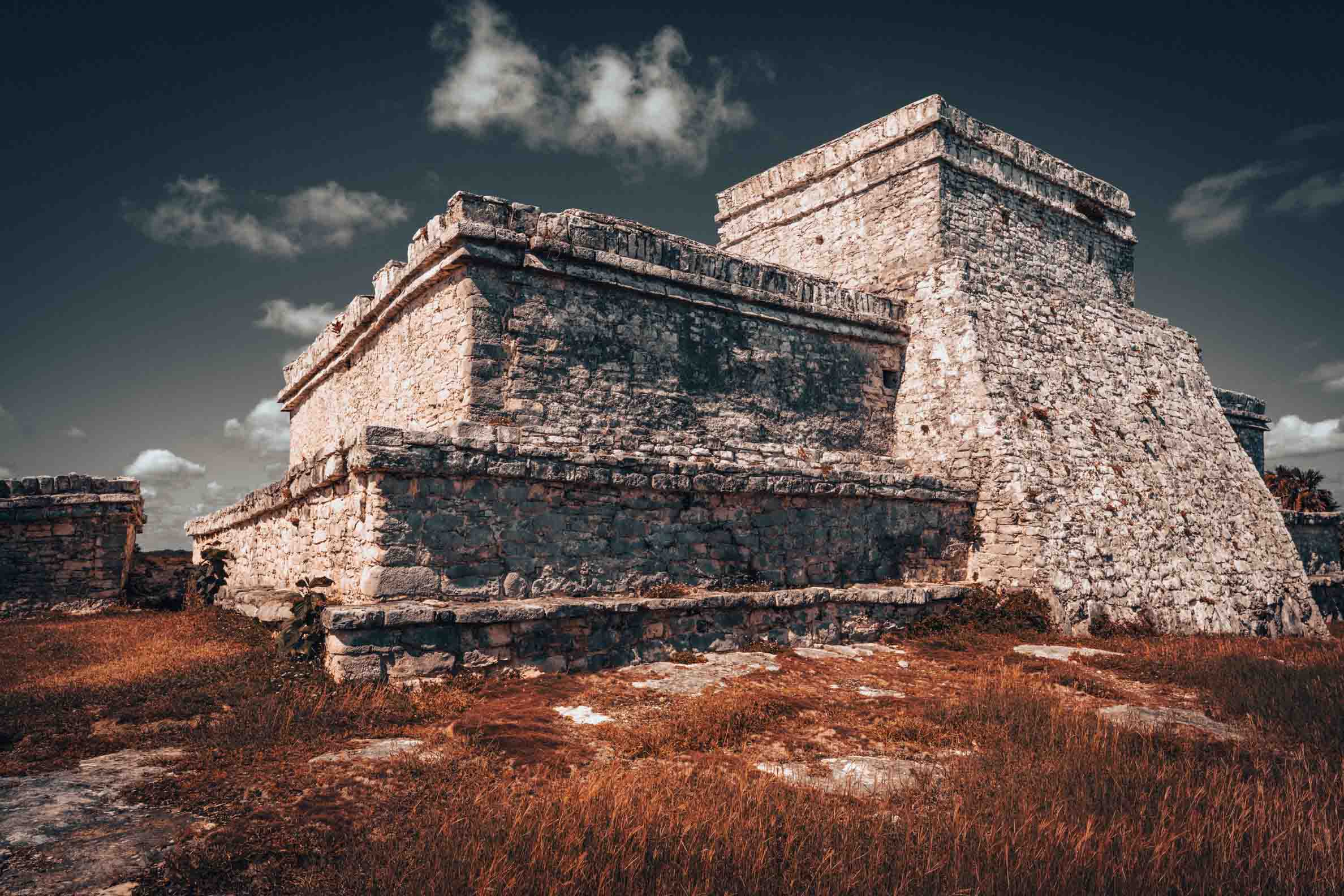 Ancient Maya limestone building at the Tulum archaeological site in Mexico, featuring weathered stone walls beneath a dramatic sky.
