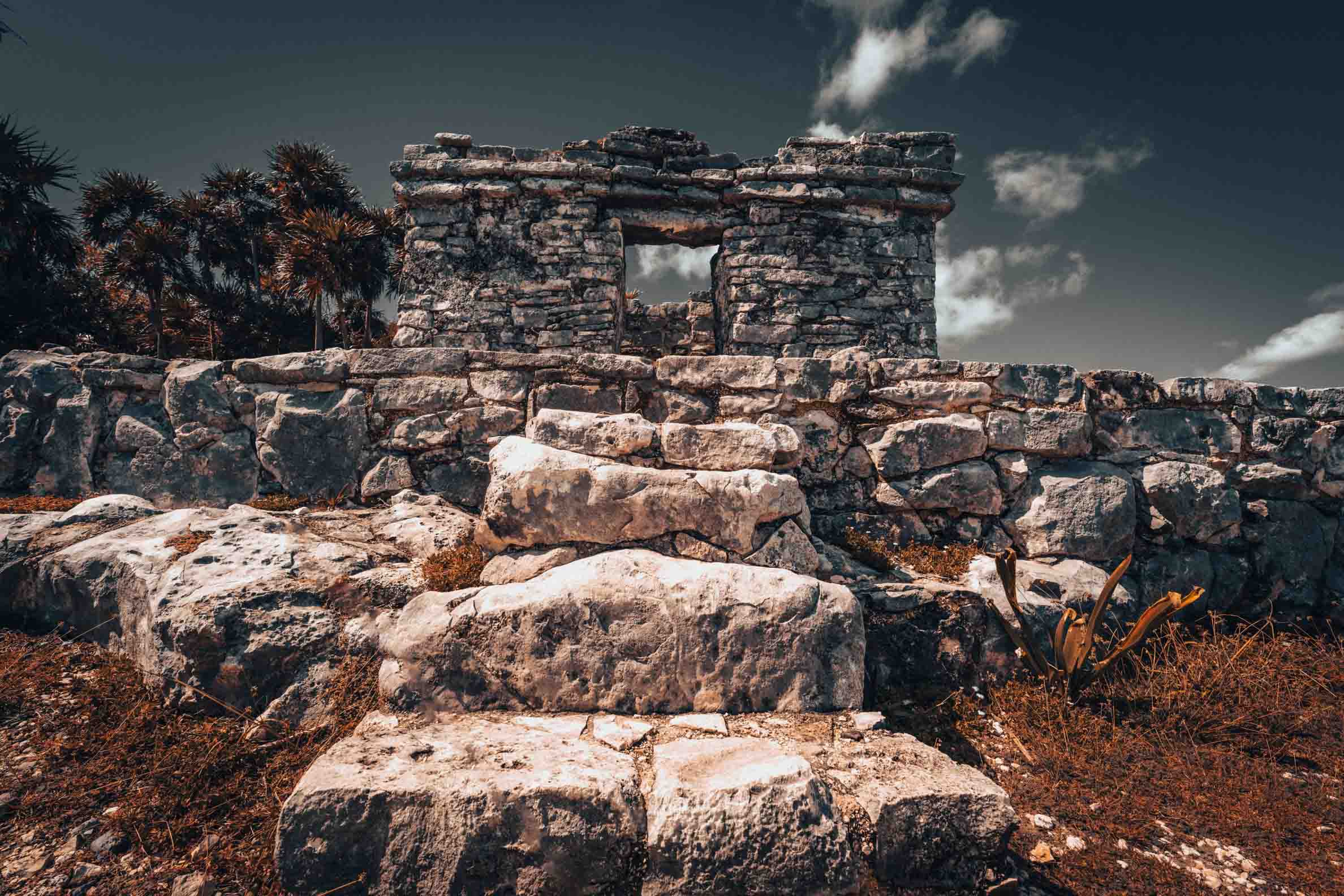 Ancient Maya stone doorway surrounded by weathered limestone ruins and tropical vegetation at the Tulum archaeological site in Mexico.
