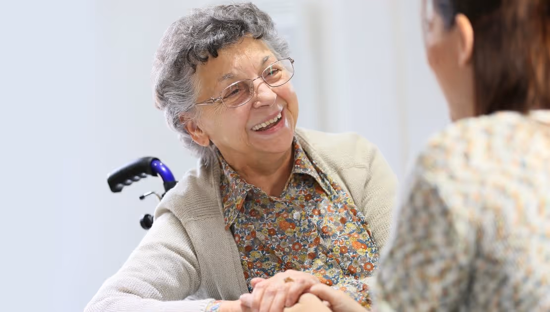 A senior dementia patient on a wheelchair, smiling to someone off-camera