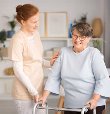 A carer happily helping a dementia patient with her walker