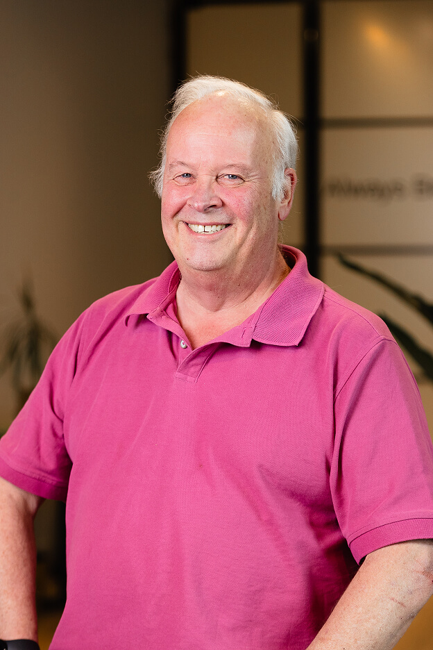 Middle-aged man with white hair wearing a pink polo shirt, standing in an office of Always Beyond Calgary IT services.