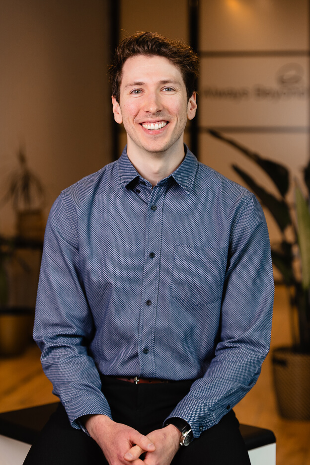 Team member wearing a blue patterned shirt sitting in an office with Always Beyond Calgary IT services logo in background.