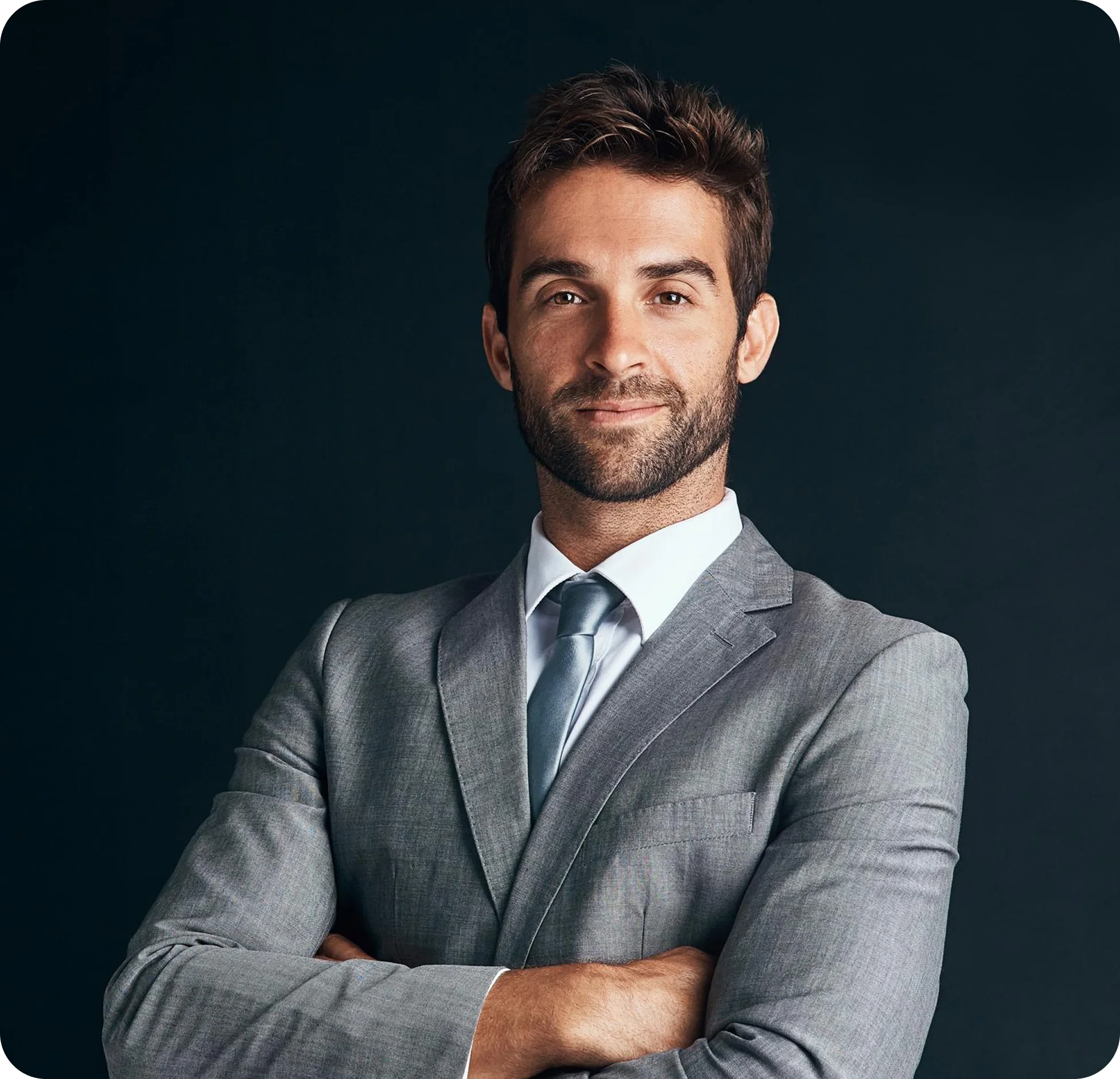 Confident man in gray suit and tie with arms crossed against dark background.