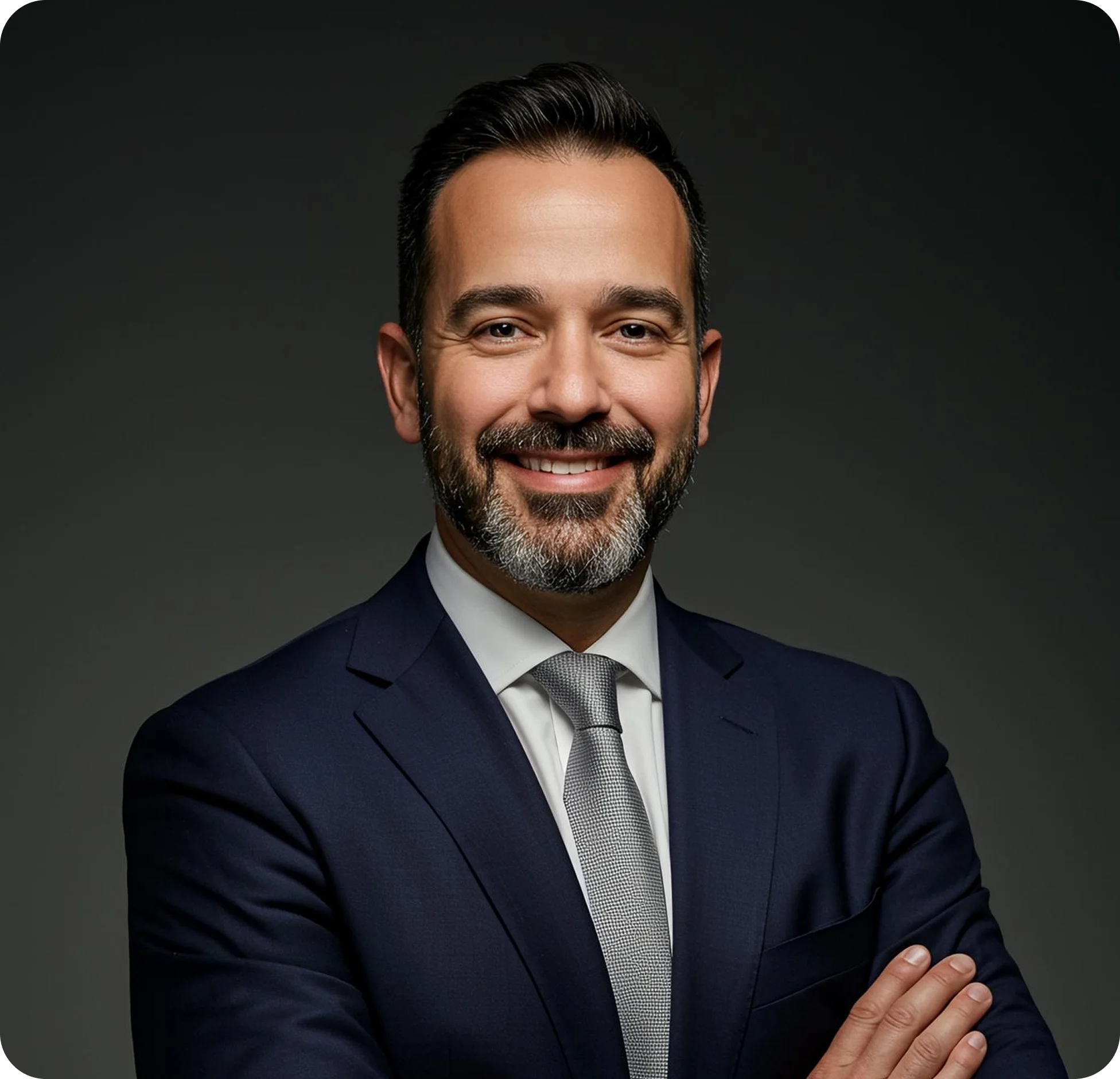 Smiling man with a beard wearing a navy suit and gray tie against a dark background.