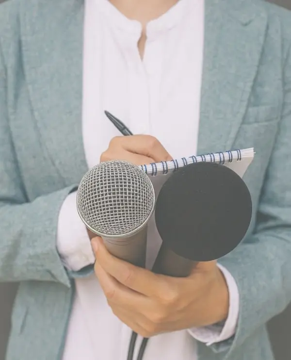 Person holding two microphones and a notepad, prepared for an interview or presentation.