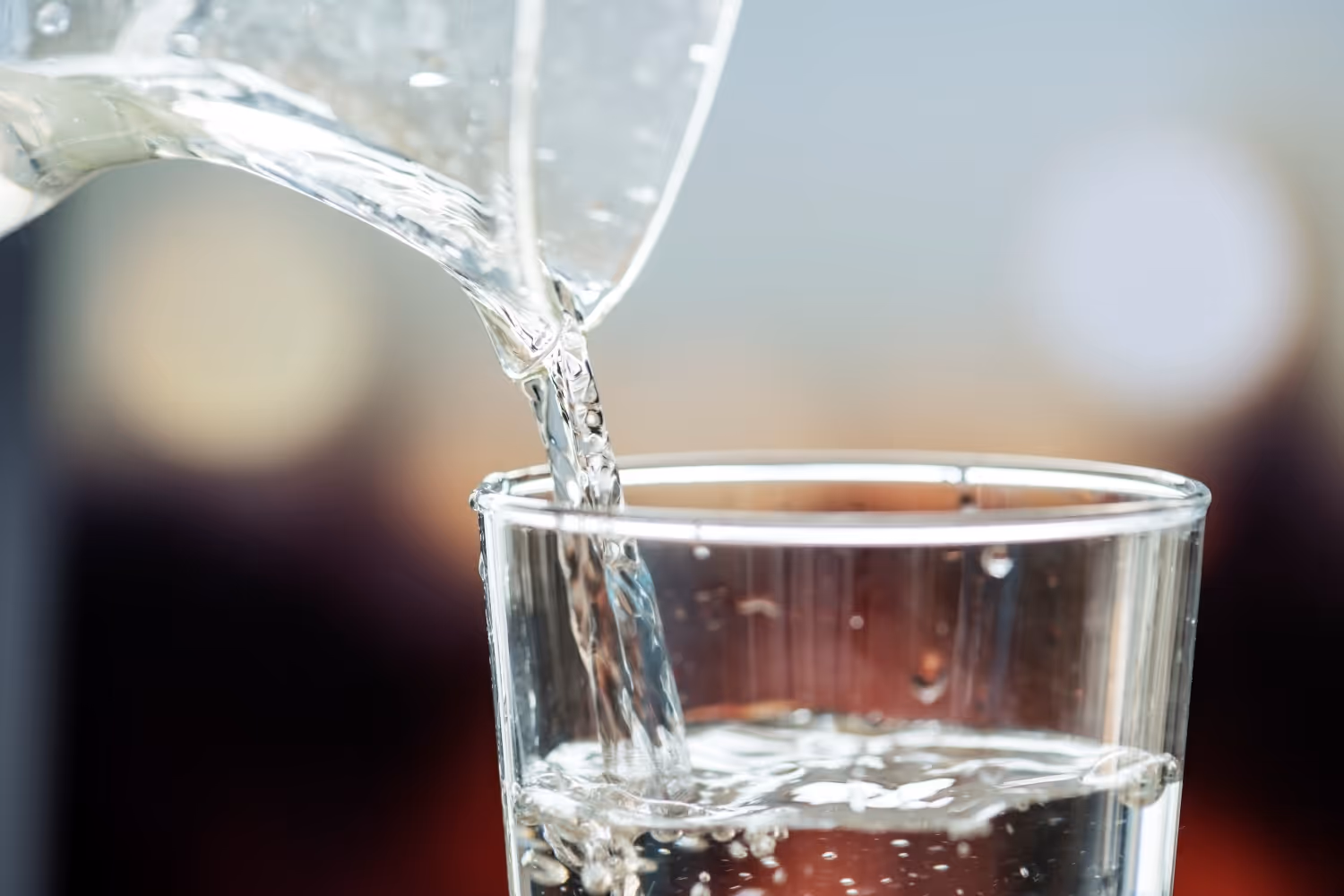Ausschnitt einer Karaffe aus der Wasser in ein Glas gekippt wird.
