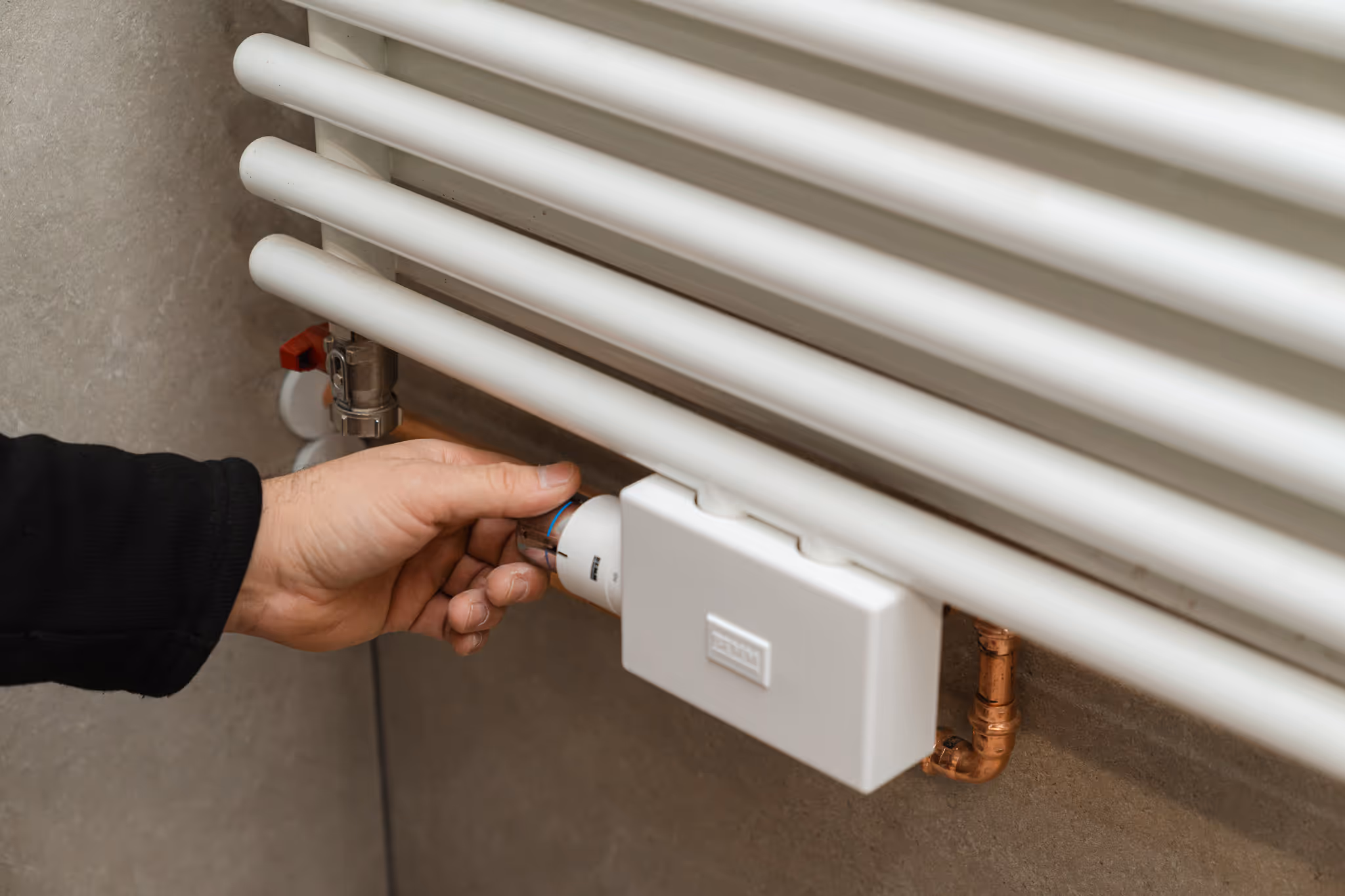 Eine Hand dreht am Thermostat eines Heizkörpers