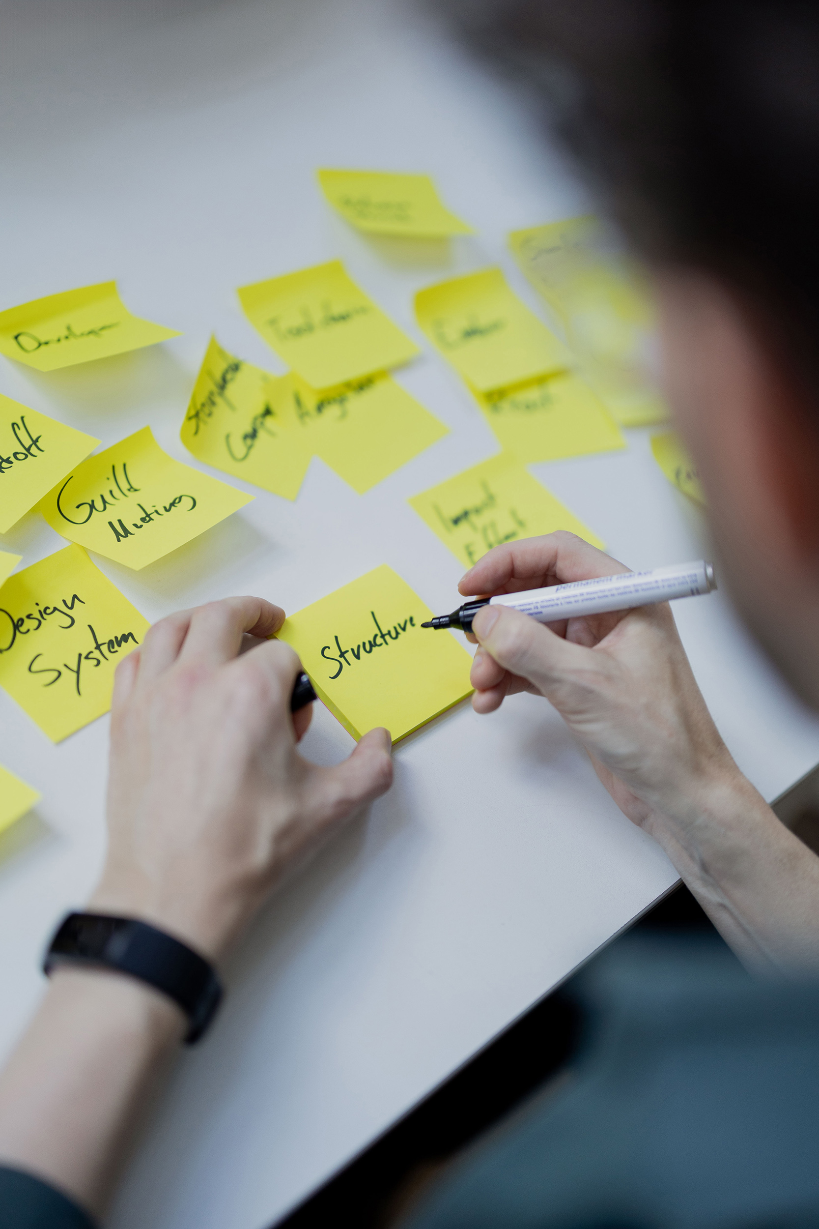 Person schreibt auf ein gelbes Postit.