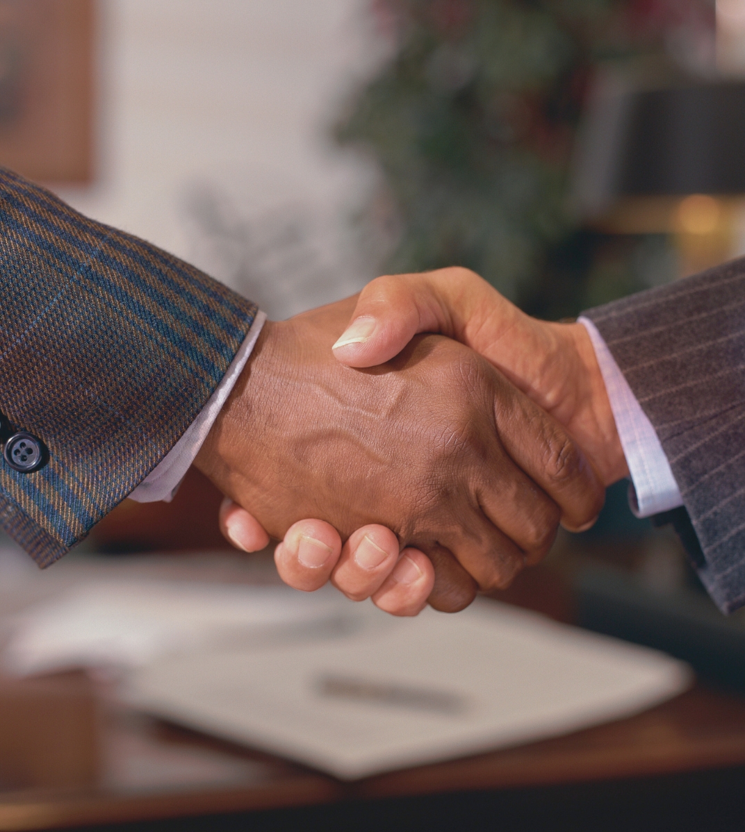 Close-up of a handshake between two people wearing business suits in an office setting.
