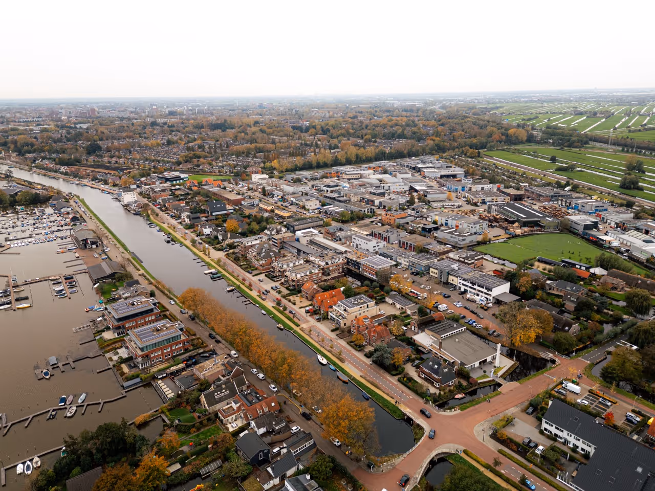 Luchtfoto van een bedrijventerrein langs het water, met gebouwen, wegen en groen in de omgeving.