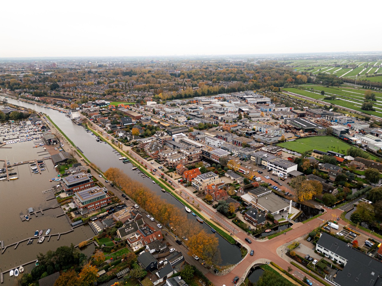 Luchtfoto van een bedrijventerrein langs het water, met gebouwen, wegen en groen in de omgeving.