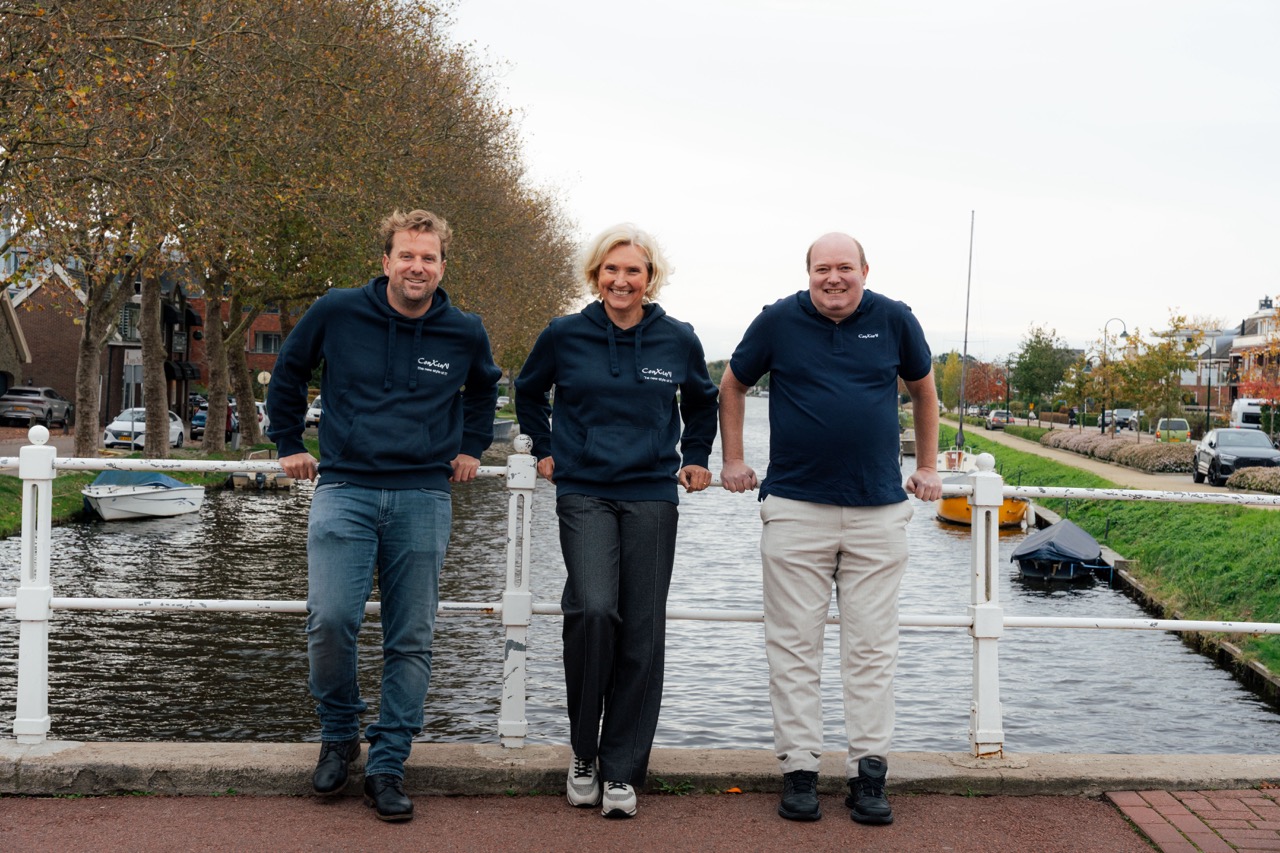 Drie ConXioN-collega’s staan op een brug langs een kanaal, met bomen en straatbeeld op de achtergrond.