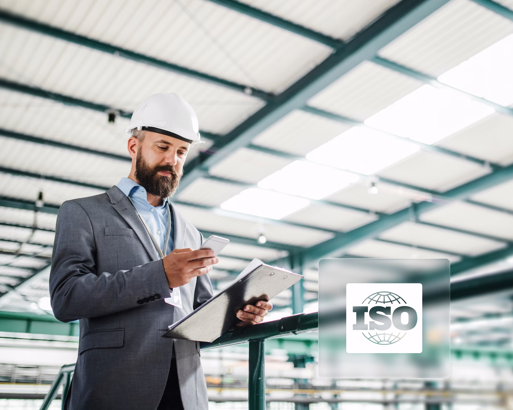 Manager mit Helm hält Telefon in der Hand in Werkshalle