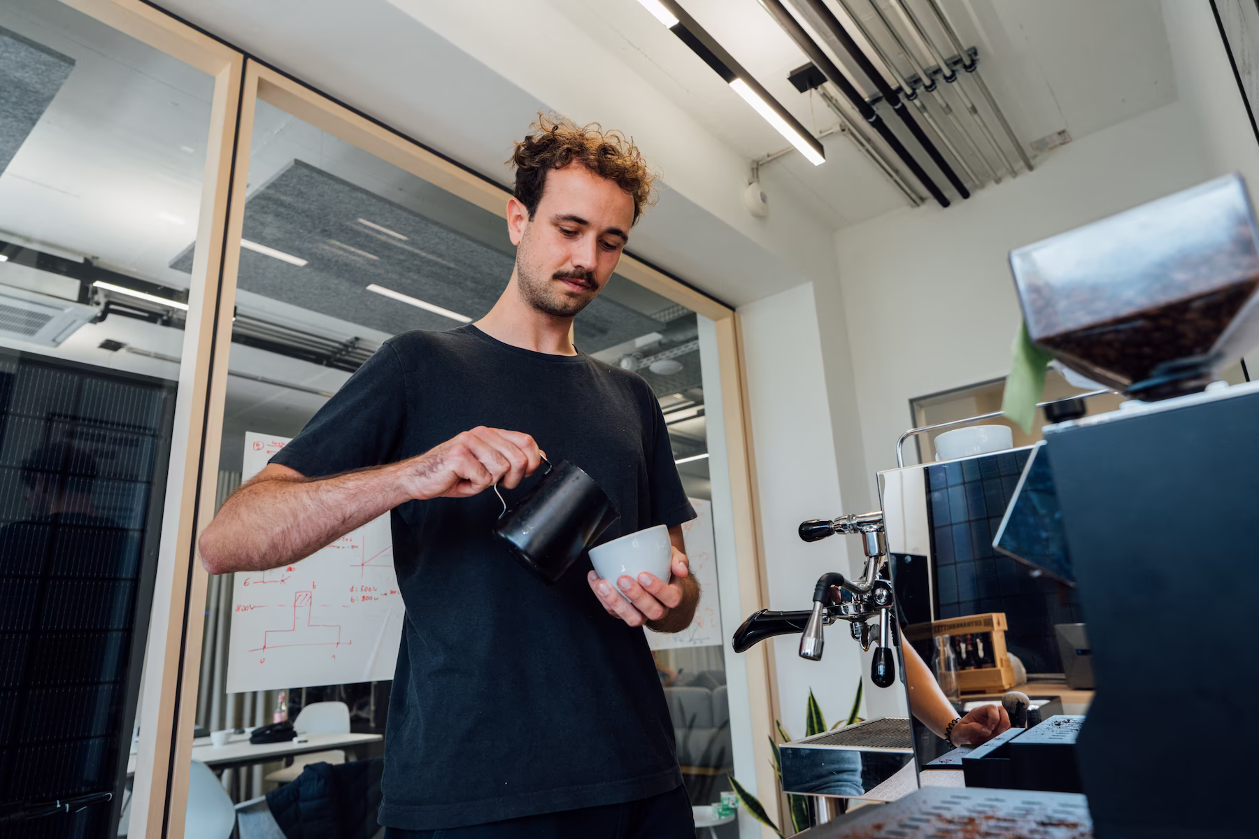 Mitarbeiter bereitet im Büro einen Kaffee an der Espressomaschine zu