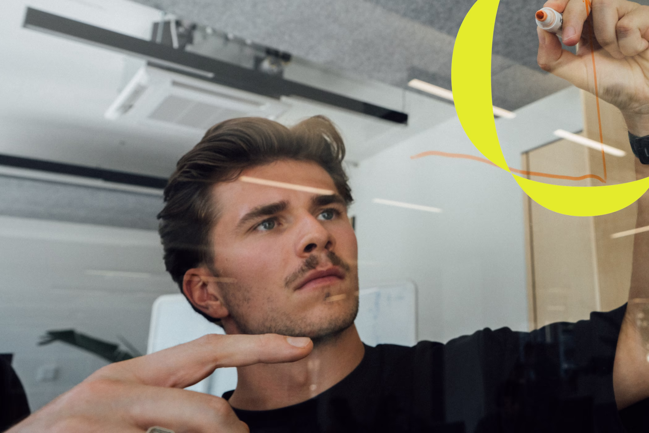 Mitarbeiter zeichnet Skizzen an einer Glaswand im Büro⁄