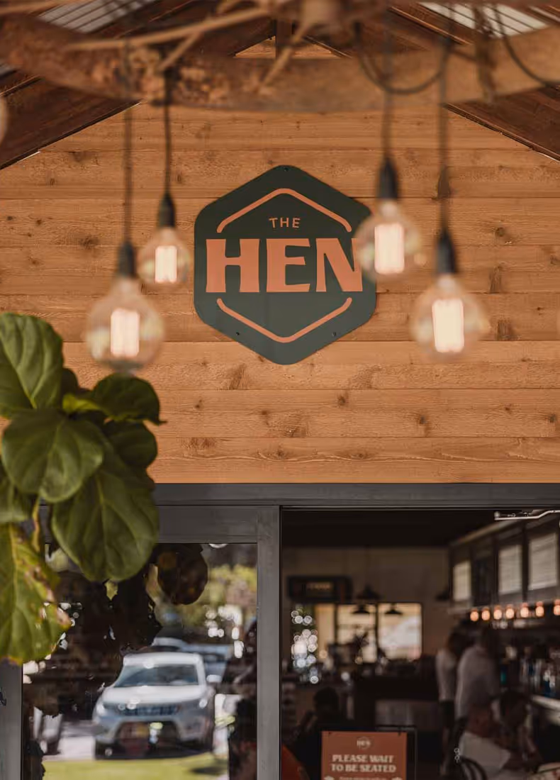 The Hen sign mounted on a wooden wall with decorative hanging lights in the foreground