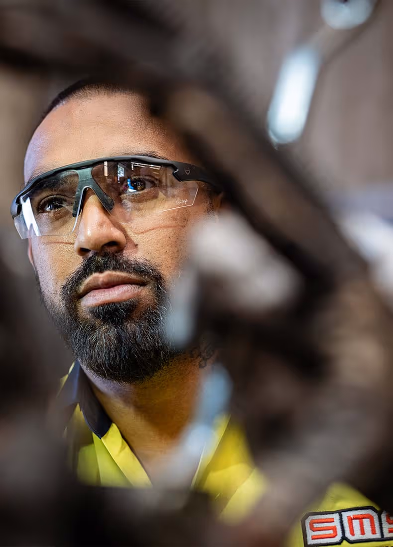 Portrait of a worker wearing protective glasses and a yellow SMS-branded hi-vis shirt, focused on a task.
