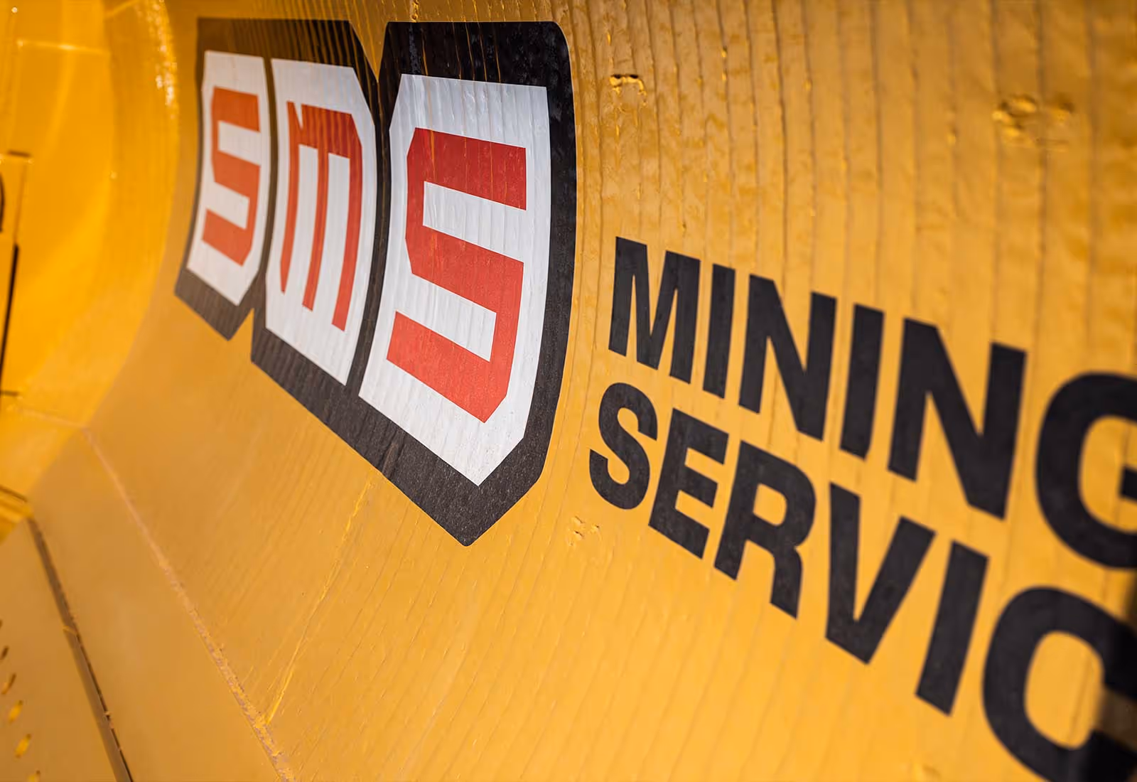 Angled close-up of the SMS Mining Services logo on yellow heavy machinery.