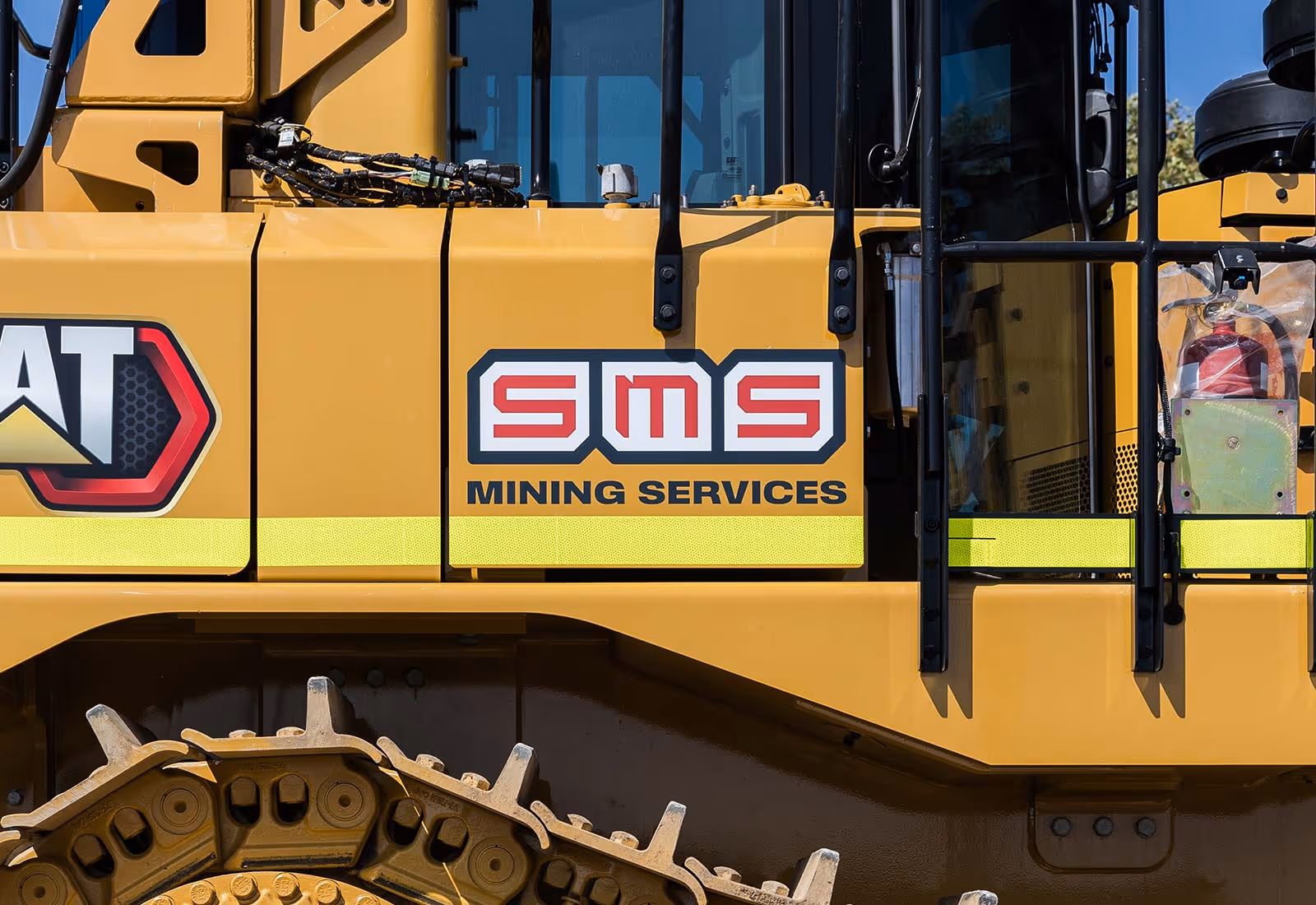 Close-up of the SMS Mining Services logo on the side of a large yellow Caterpillar mining vehicle.