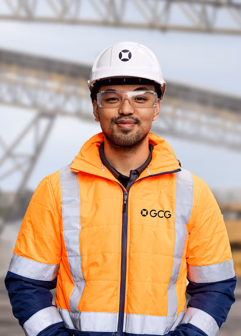 GCG worker wearing orange high-visibility jacket, white safety helmet, and safety glasses on an industrial site