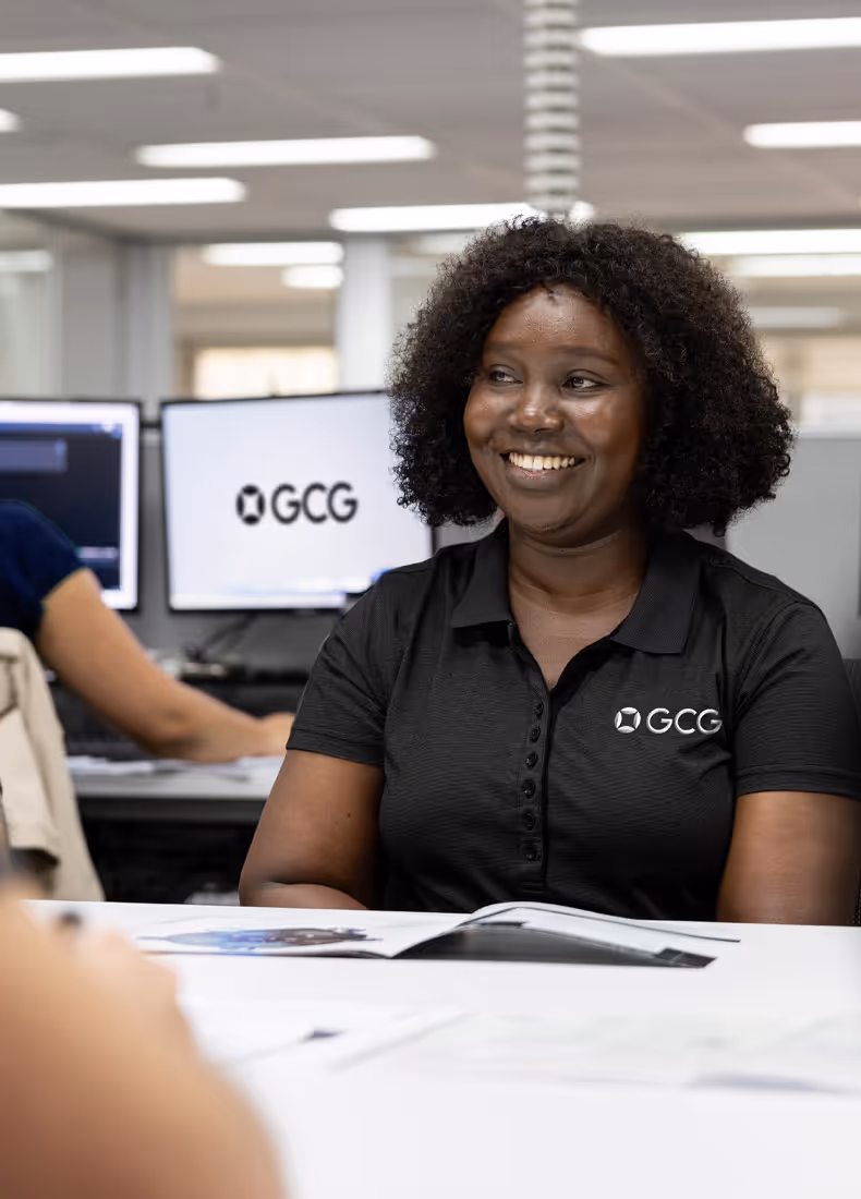 Smiling GCG employee wearing black branded polo shirt, seated in an office meeting