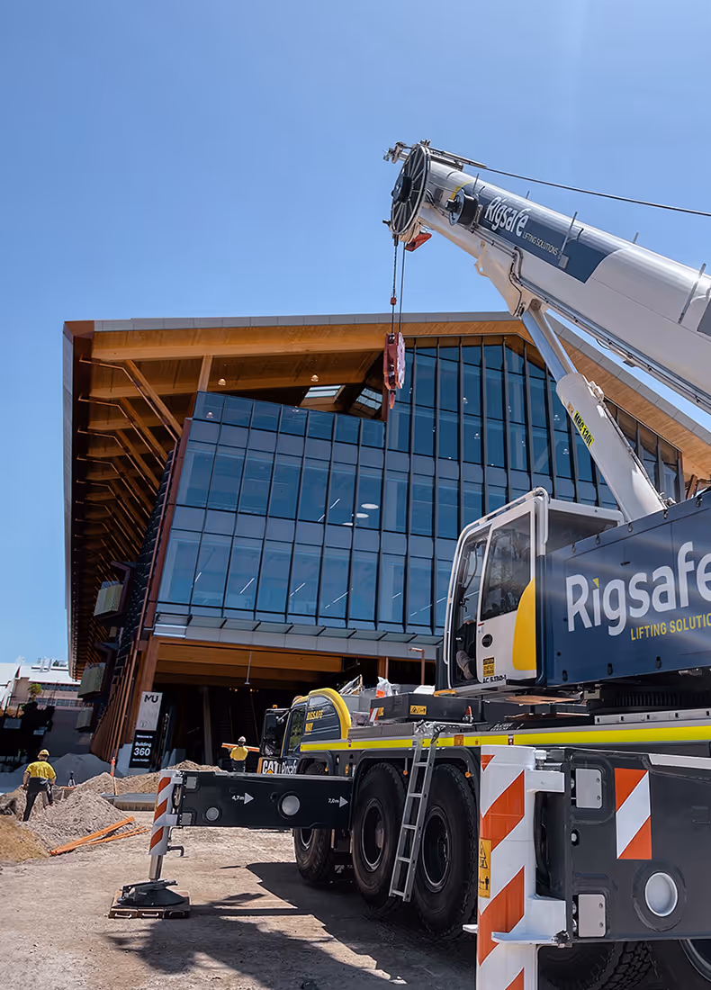 Close-up of Rigsafe crane operating in front of a glass-fronted building under blue sky