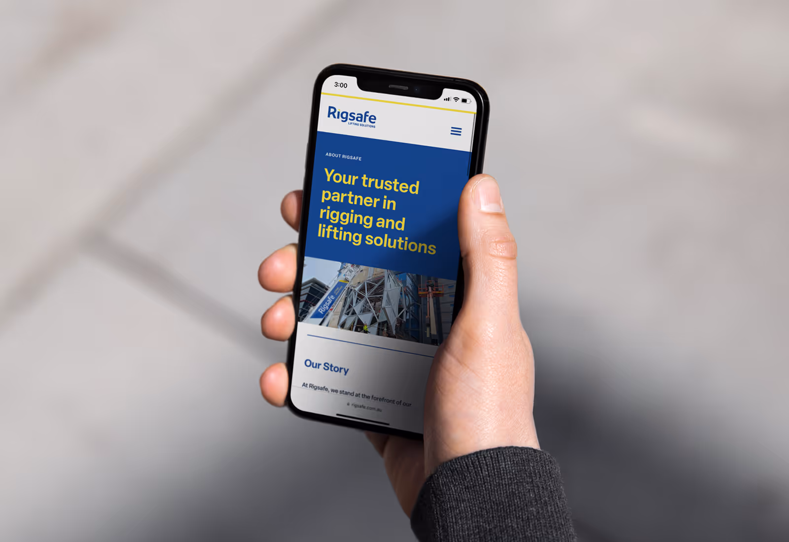 Person holding smartphone showing Rigsafe website homepage with rigging and lifting solutions tagline